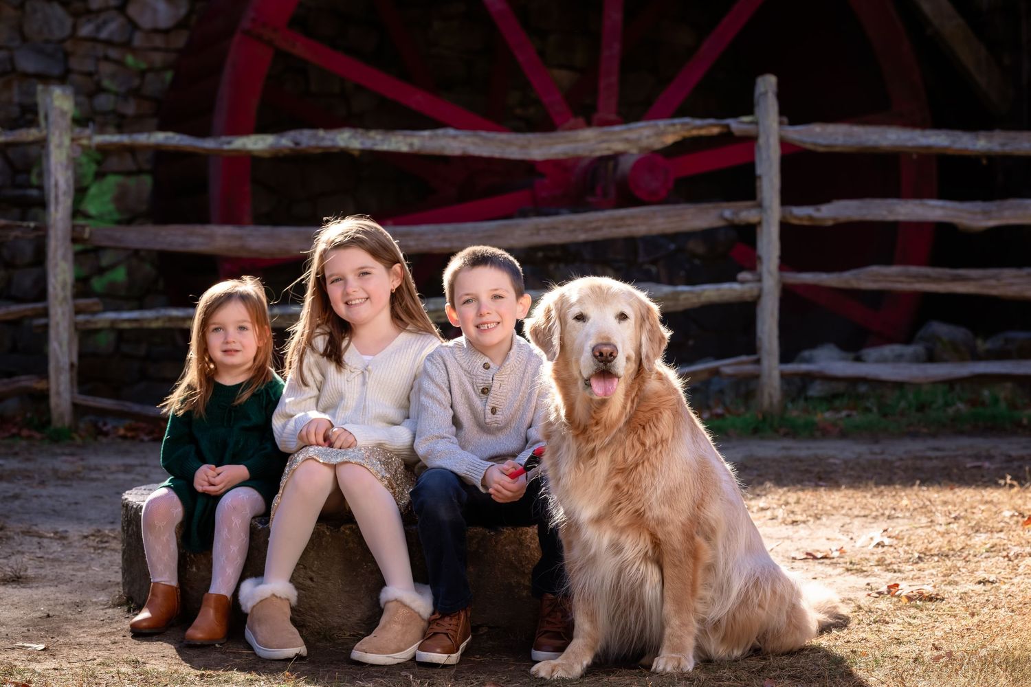 A golden retriever sits with a group of people on a wooden bench outdoors.