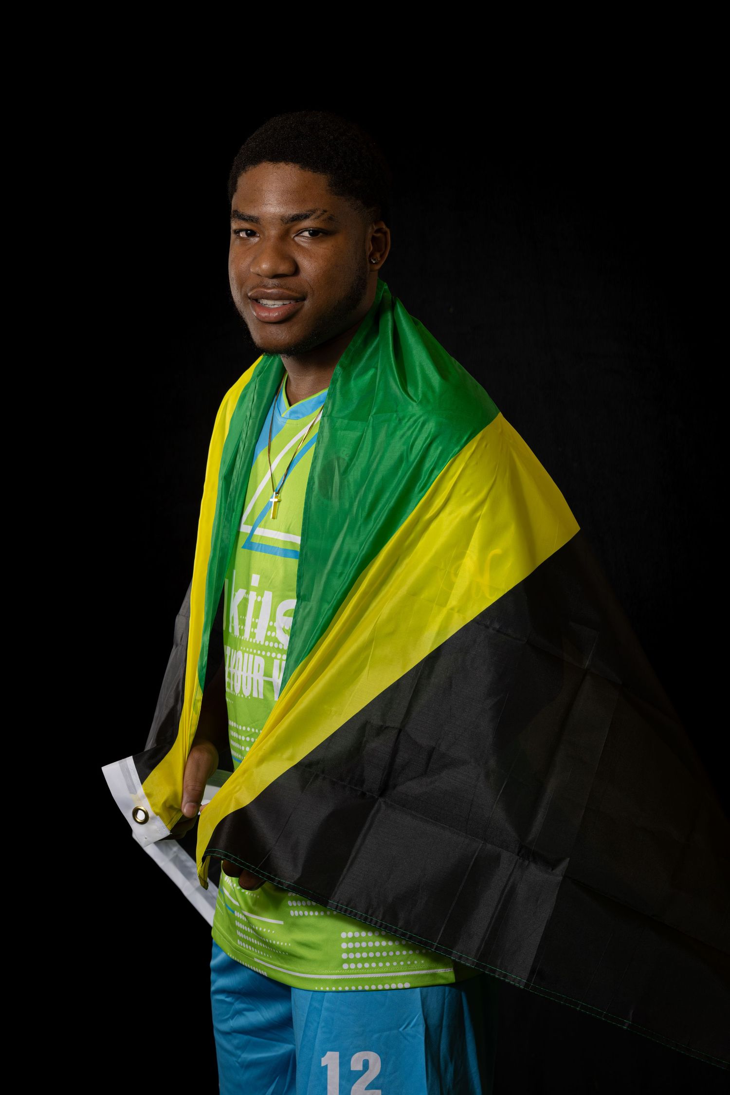 Athletic figure wearing a vibrant green and yellow jersey with number 12 poses against dark background.