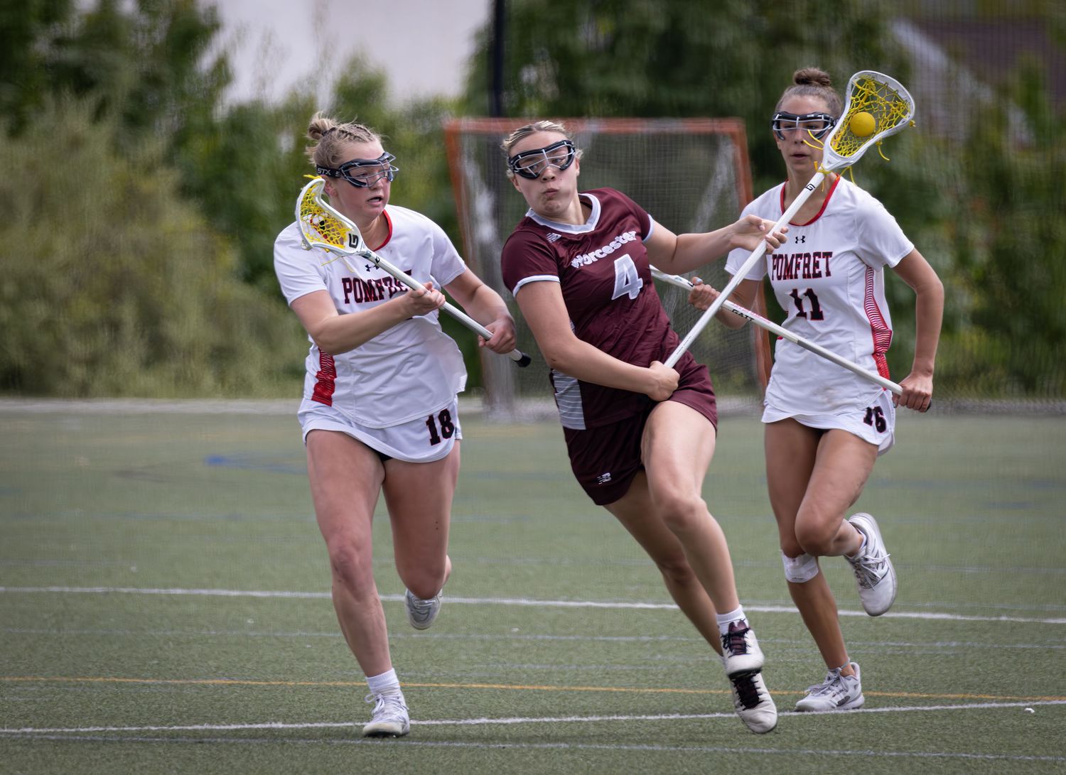 Women's lacrosse players compete for possession of the ball during an intense match between maroon and white teams.