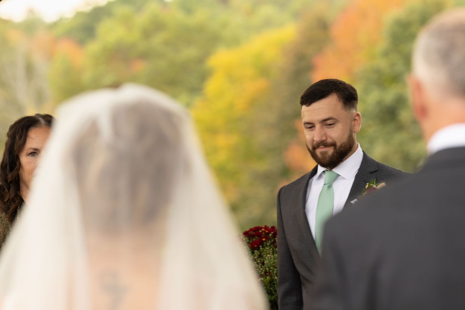 Outdoor autumn wedding ceremony with colorful fall foliage in the background and emerald green tie detail.