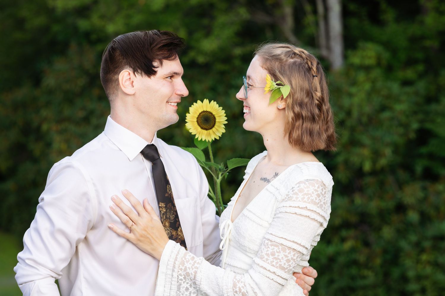 A couple in white wedding attire shares romantic moments in a garden setting with sunflowers.