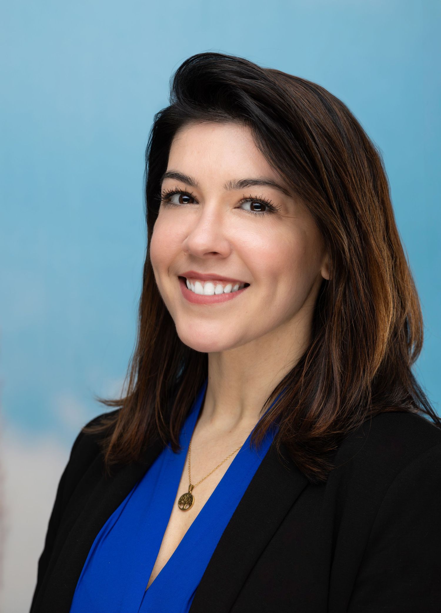 Professional headshot series of a person in business attire with a black blazer and royal blue top against a light blue backdrop.