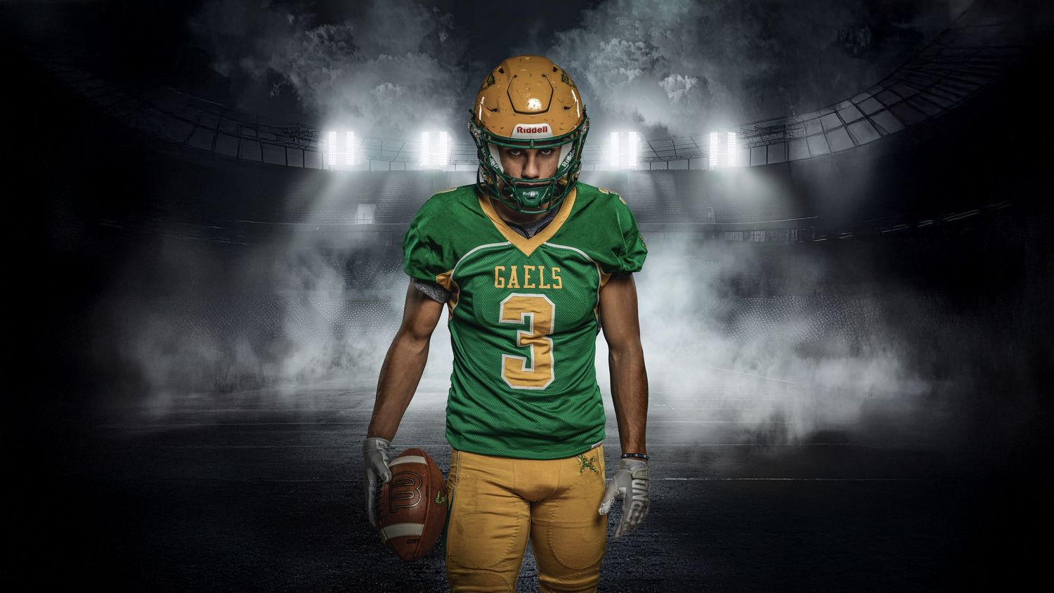Football player in green and gold uniform stands holding ball against dramatic smoky stadium backdrop with bright lights.