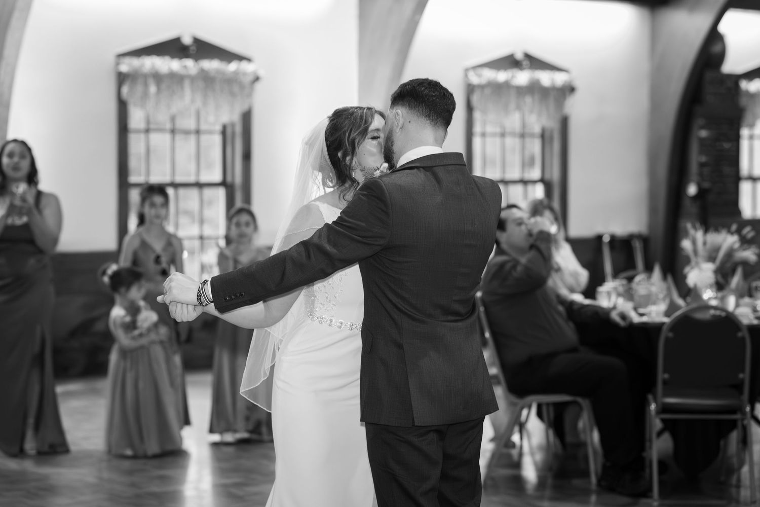 A bride and groom share their first dance at a wedding reception in a classic black and white photograph.