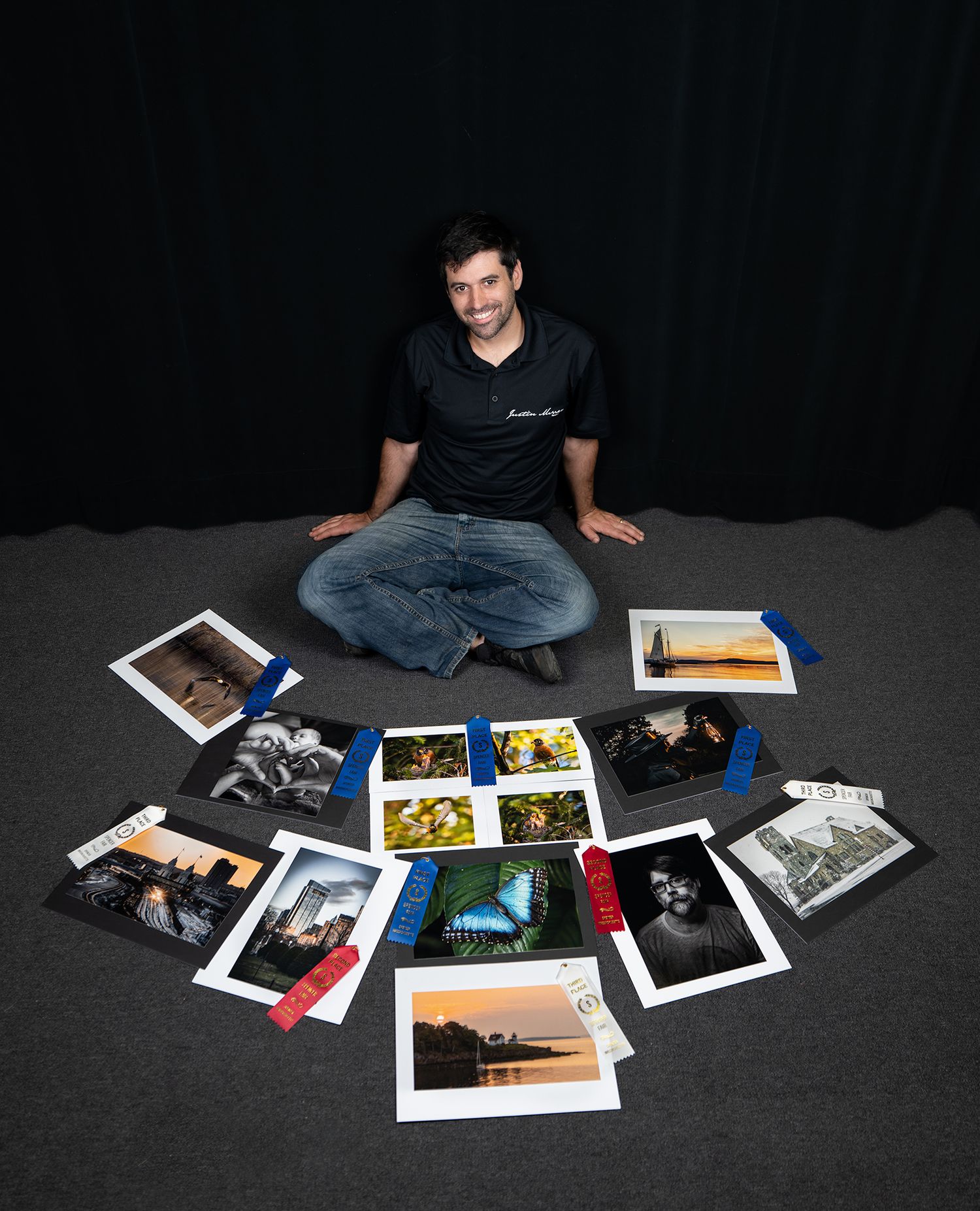 A series of photographs spread out on a dark floor with someone sitting cross-legged viewing them in low light.