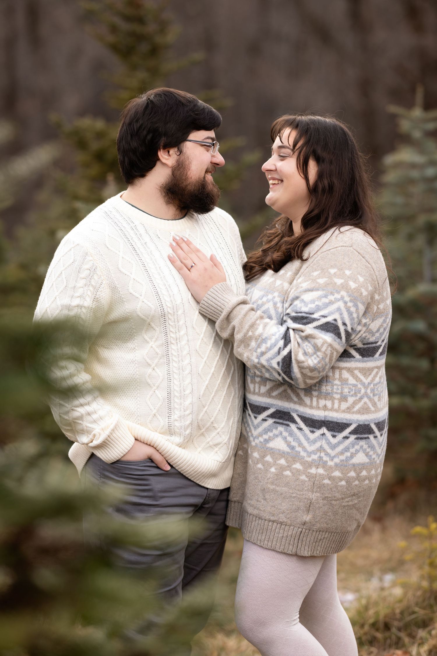 A couple in cozy sweaters share playful moments together in a natural outdoor setting during a photo session.