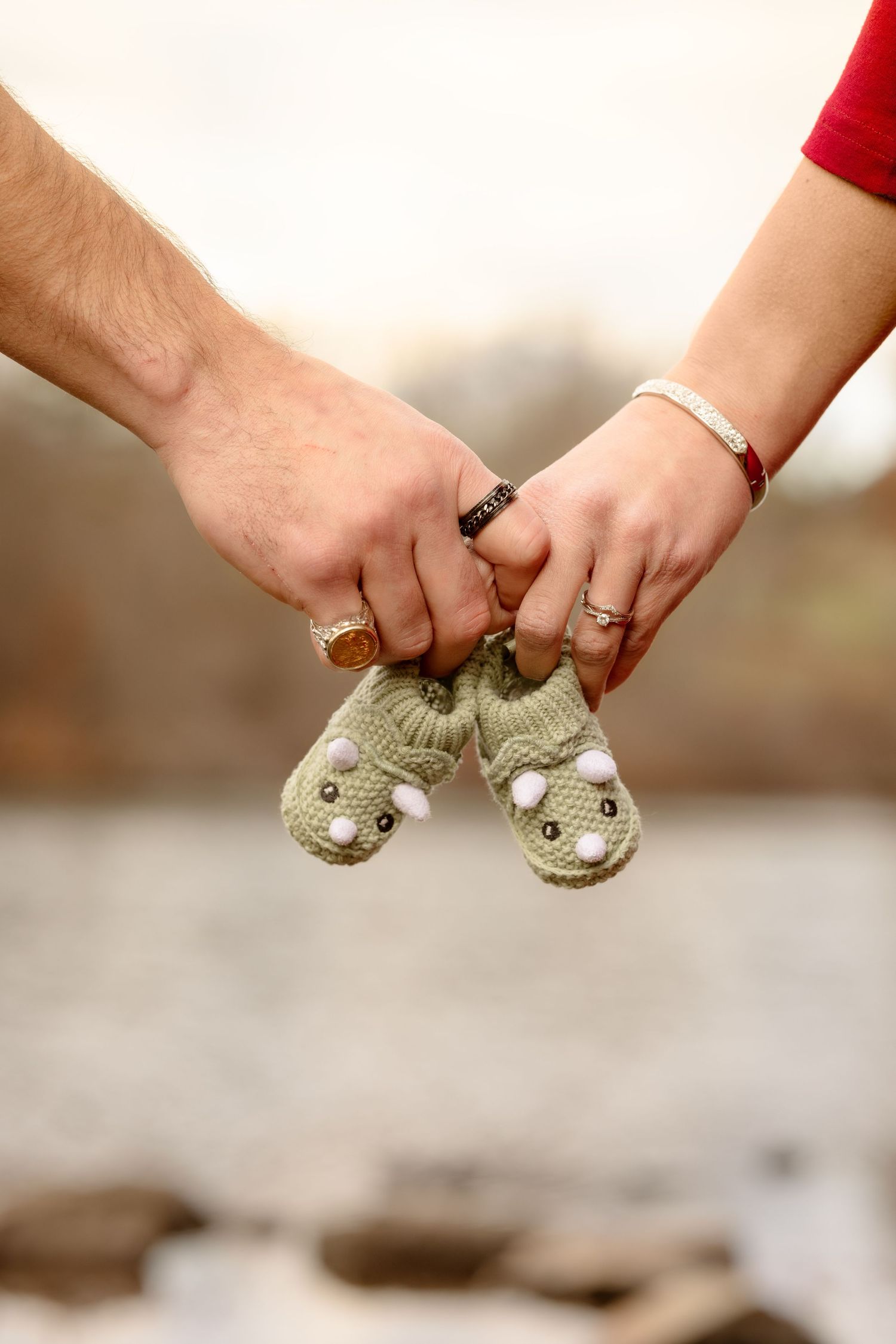 Hands holding two matching knitted owl booties against a blurred neutral background.