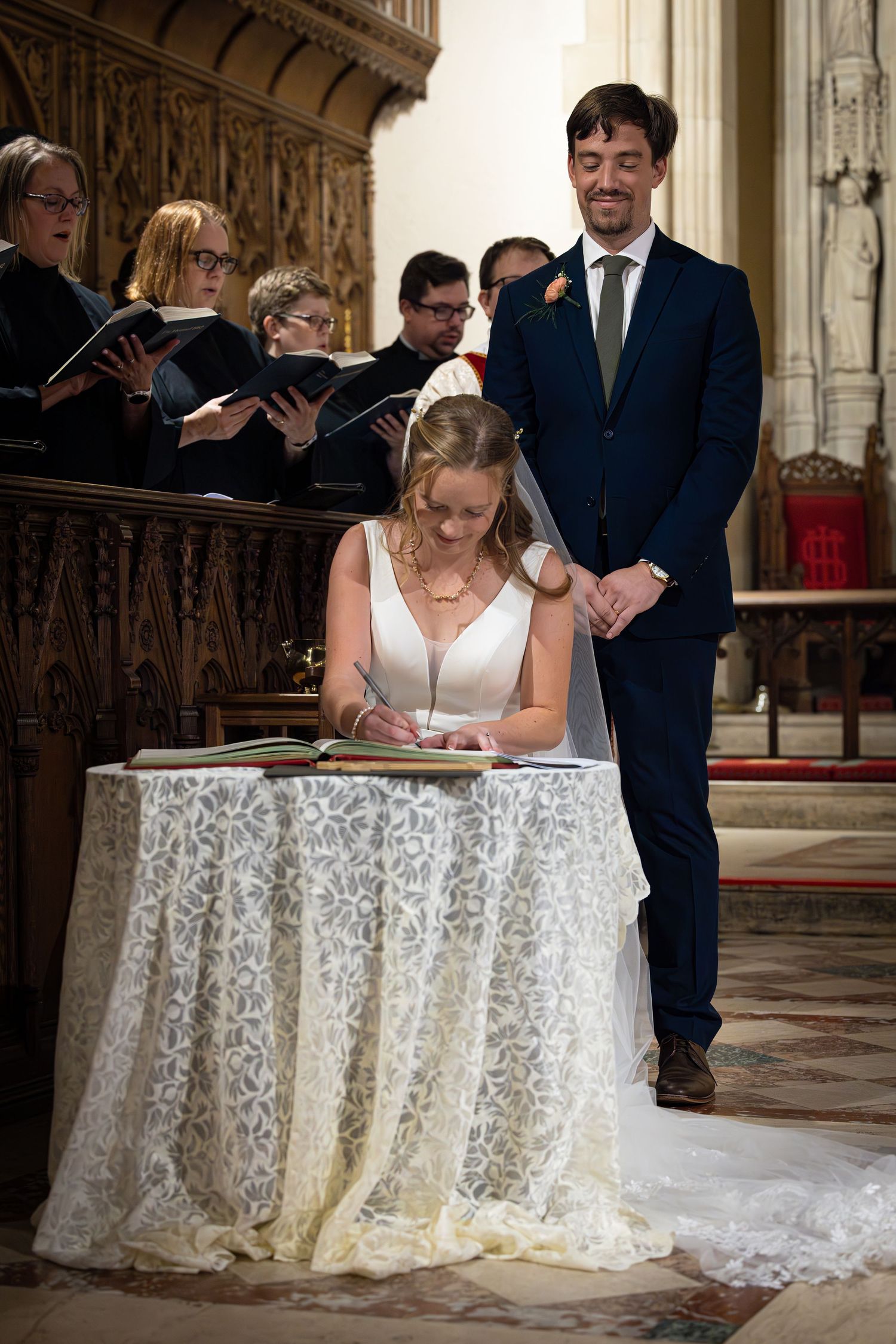 A couple signs documents on an ornate lace-covered table inside a grand church during a wedding ceremony.