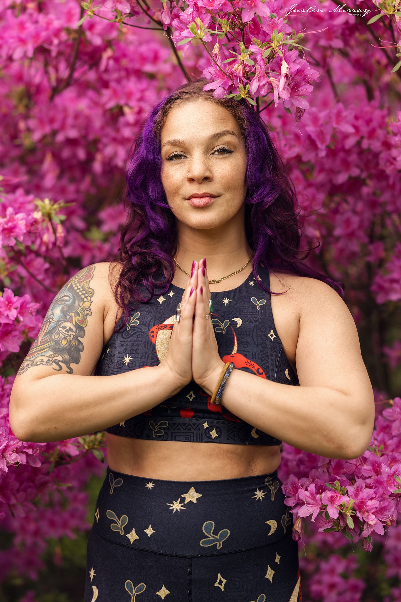 A person in a navy dress with gold stars poses in front of vibrant pink cherry blossoms.