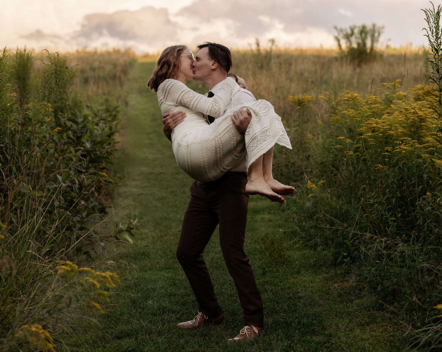 A romantic embrace in a wildflower meadow at sunset with tall grass and golden light surrounding the couple.