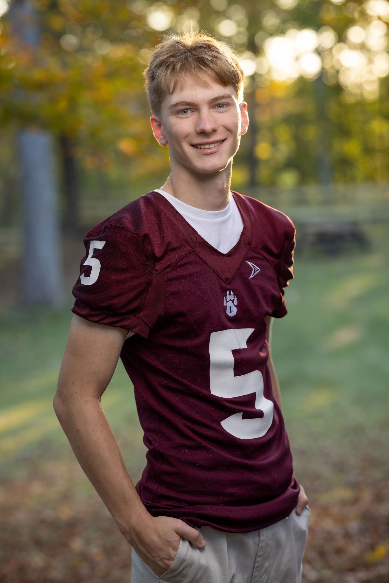 Maroon football jersey number 5 displayed in outdoor setting with fall foliage.