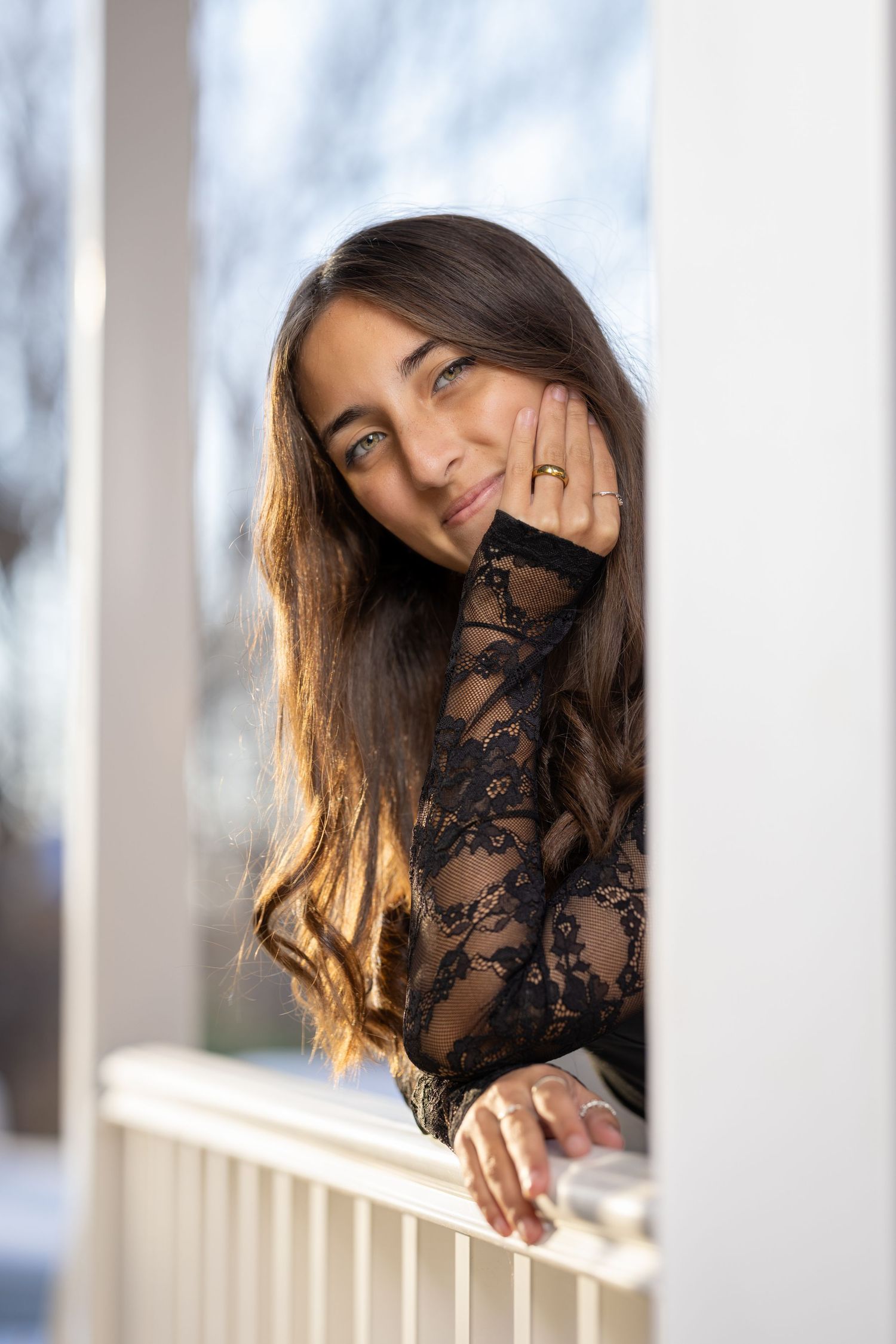 Person in black lace top posing near white window columns with soft natural lighting.