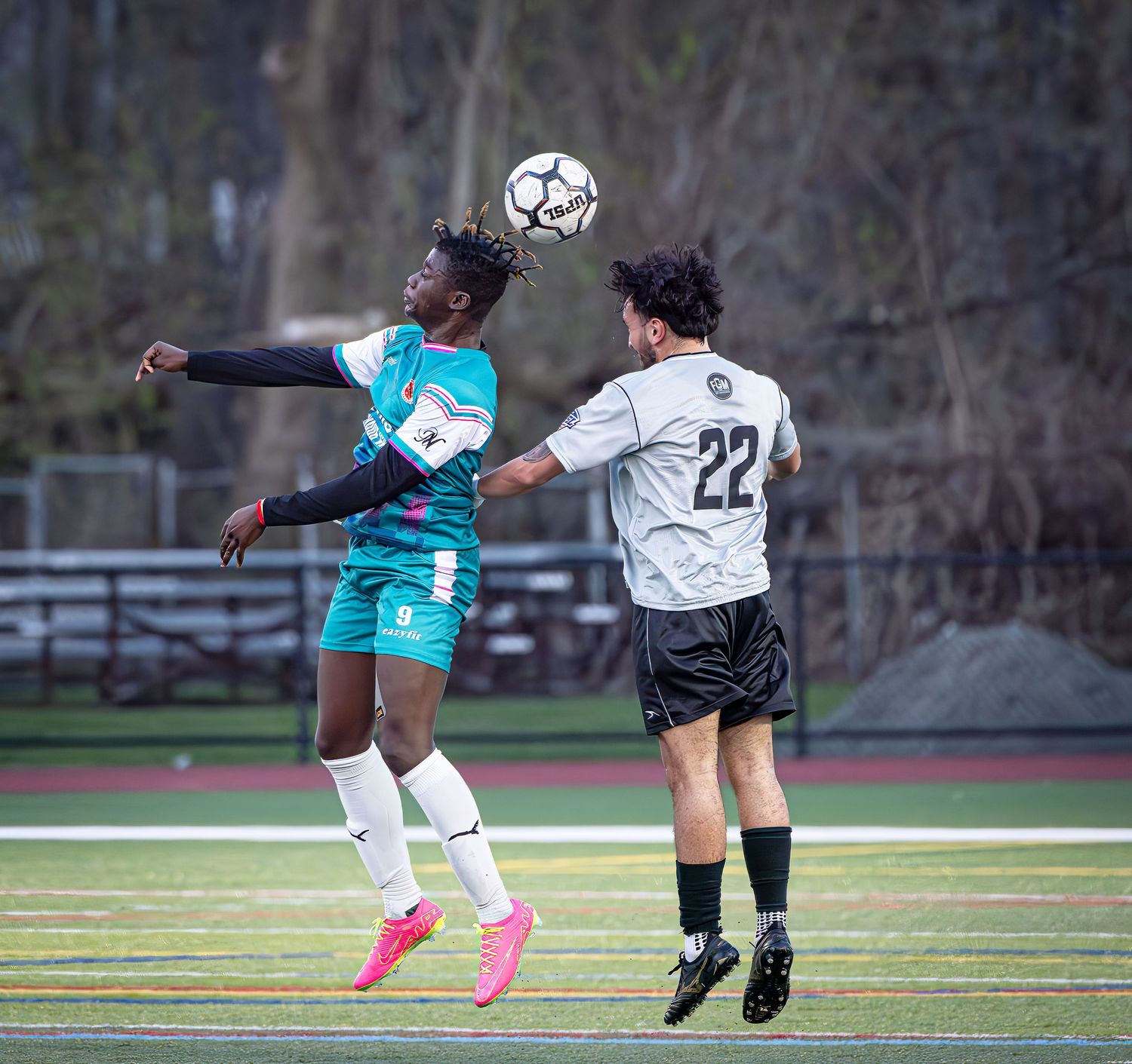 Soccer players jump high to compete for a header during an intense match on an outdoor field.