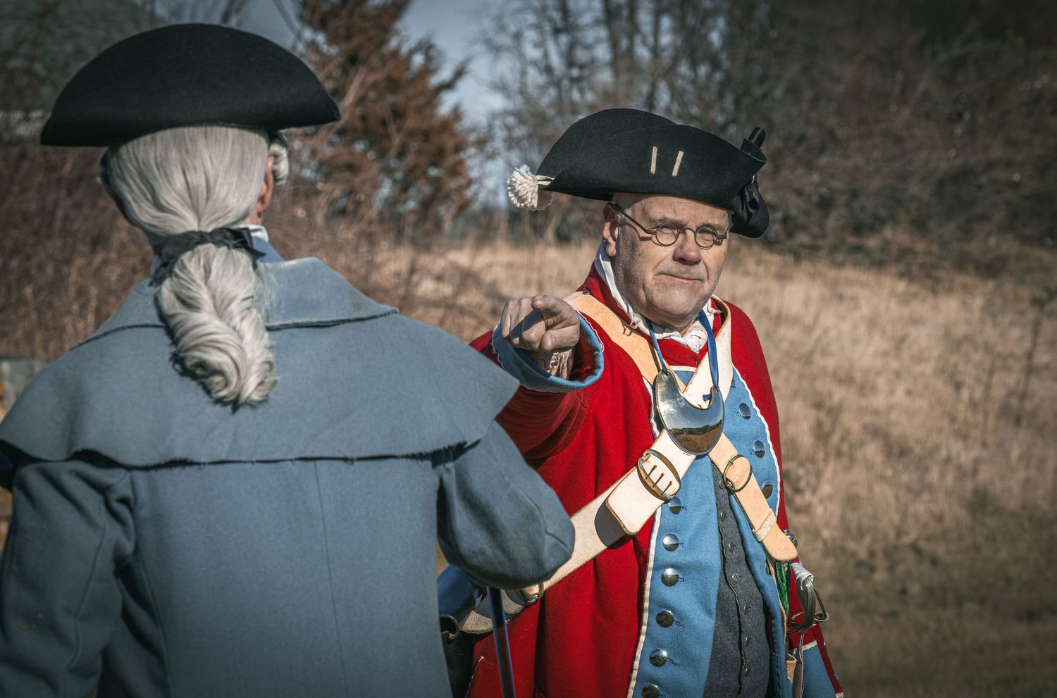 Historical reenactor in British redcoat military uniform demonstrates musket loading techniques at outdoor event.