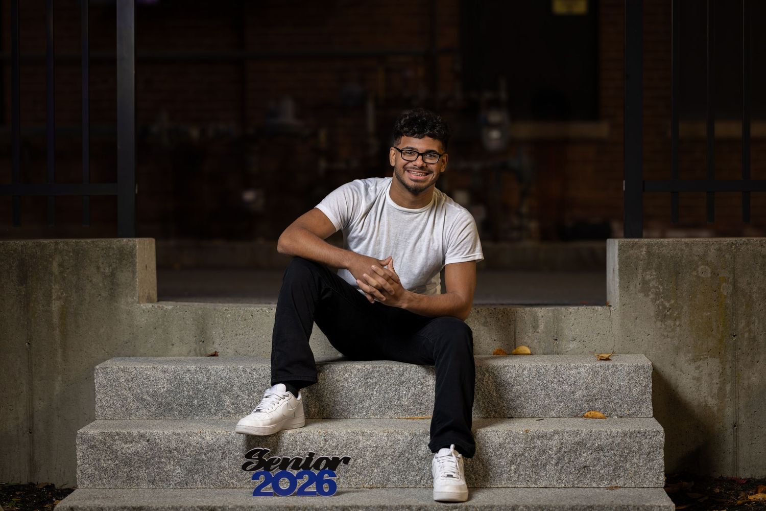 A person sits casually on concrete steps outside a building in casual attire during daytime.