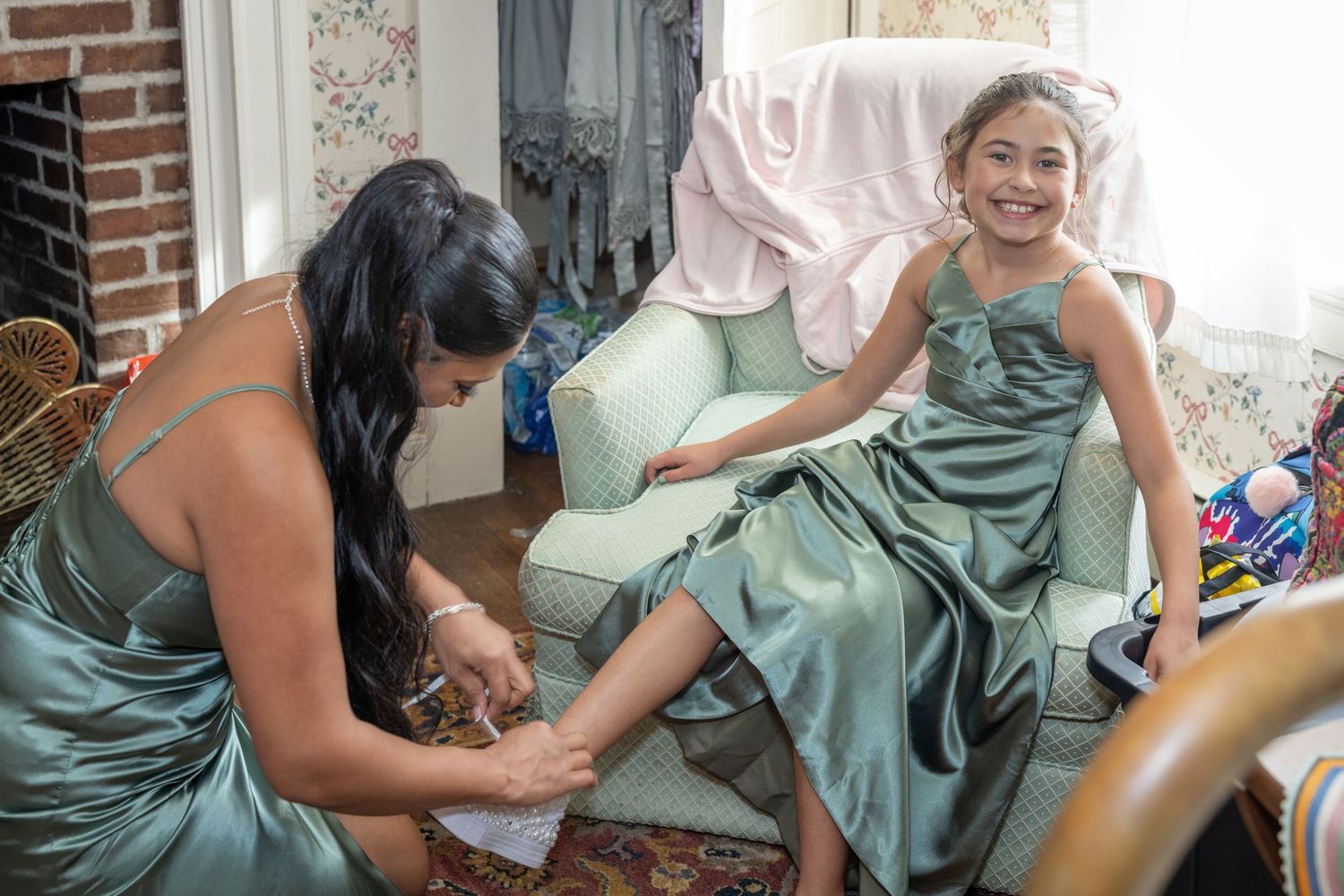 A person in a teal dress sits on a couch while receiving a leg massage during a home spa treatment.