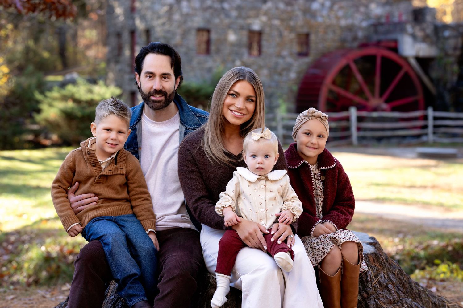 A family enjoys a casual autumn photo session outdoors with warm lighting and fall foliage in the background.