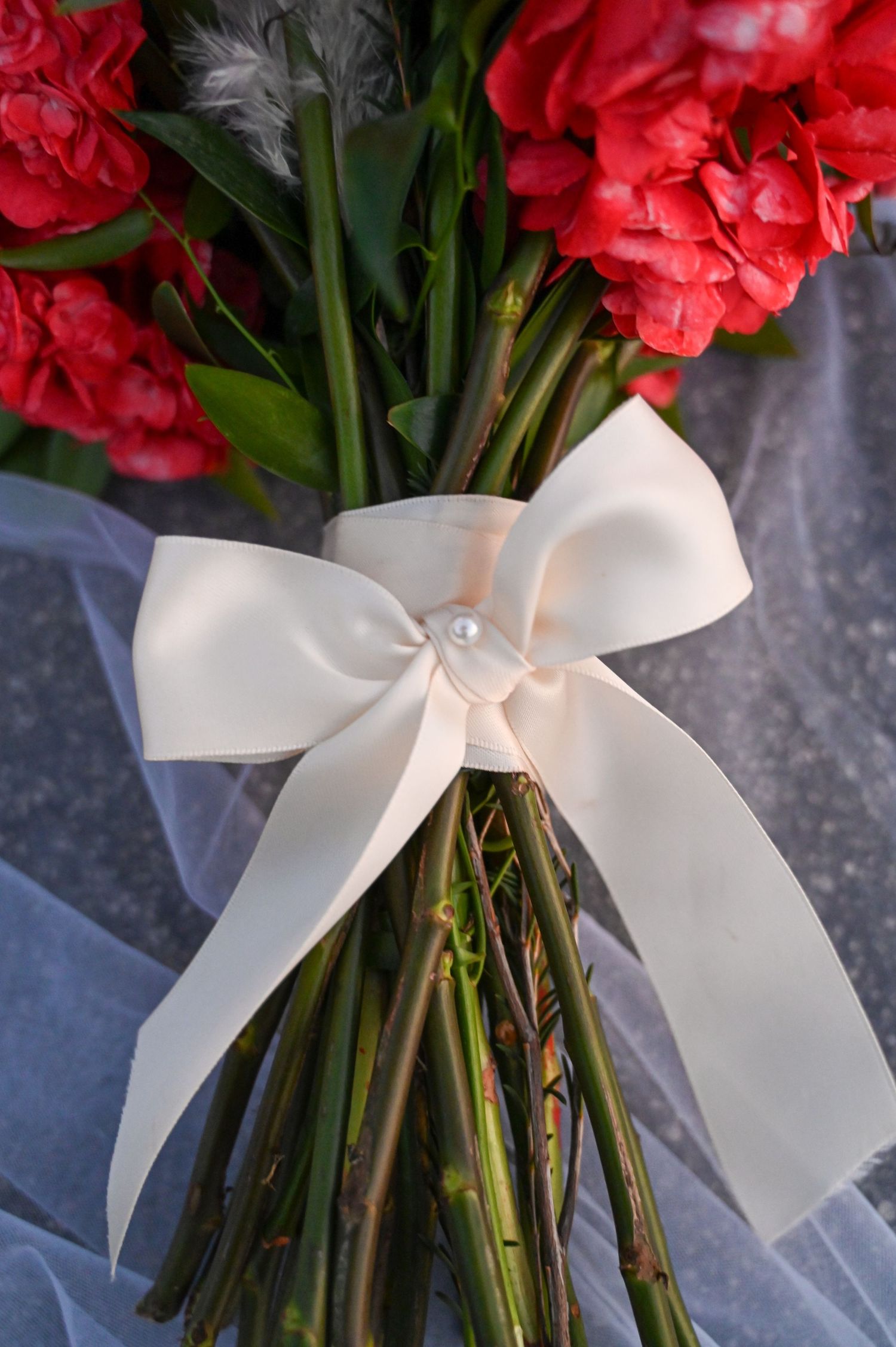 Close up of red carnation bouquet wrapped with large white satin bow.