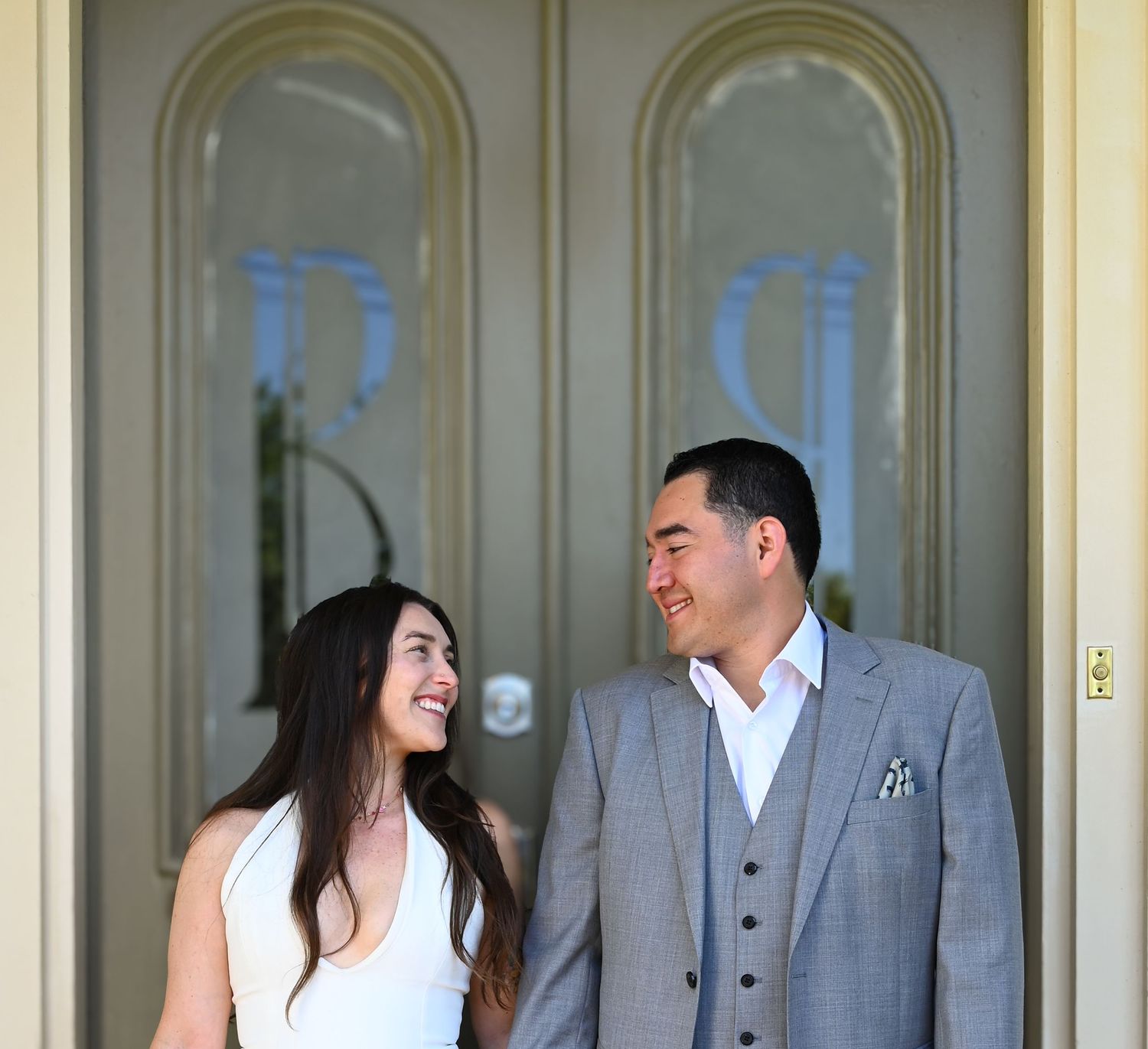 Newlyweds share a candid moment in front of elegant cream-colored doors.