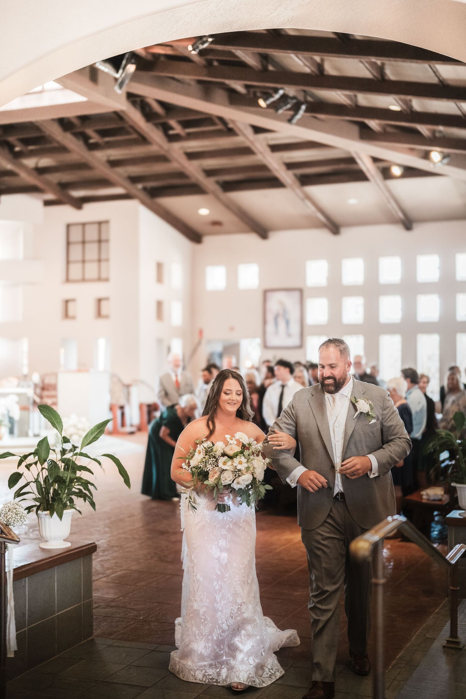 Wedding couple walking down aisle in rustic church venue with wooden beams.