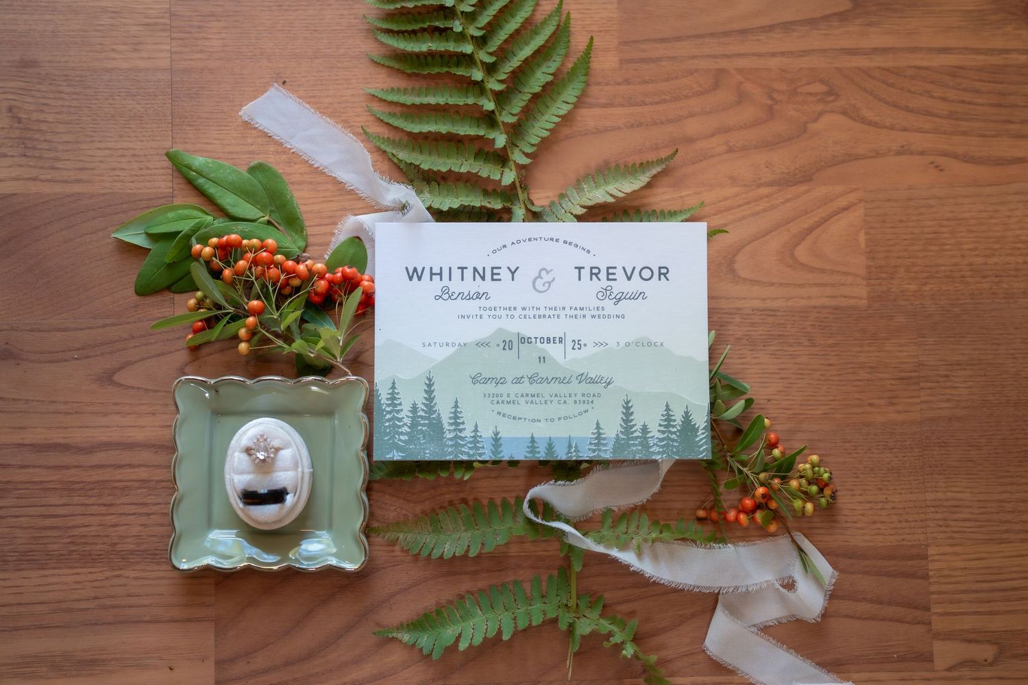 Wedding stationery with forest theme and green fern leaves on wooden surface.