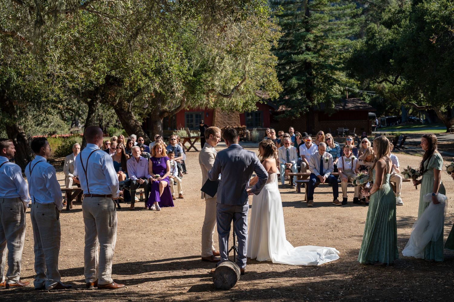 A panoramic view of an outdoor wedding ceremony with guests gathered in a scenic wooded setting during a sunny day.