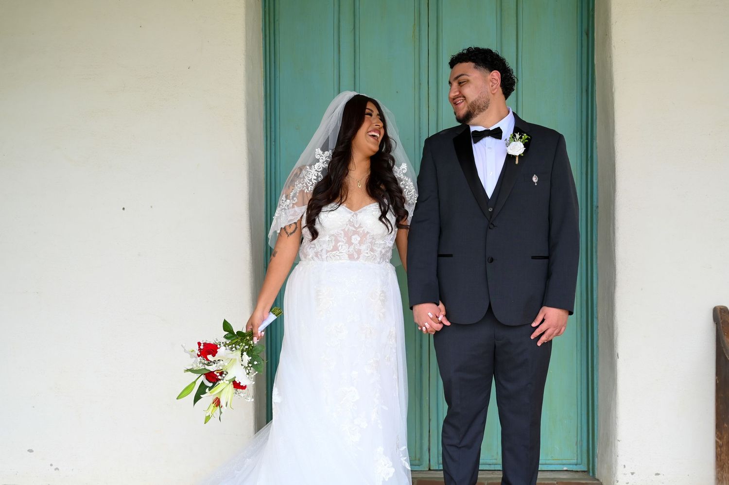 A wedding couple stands together in front of a turquoise door in a romantic outdoor setting.
