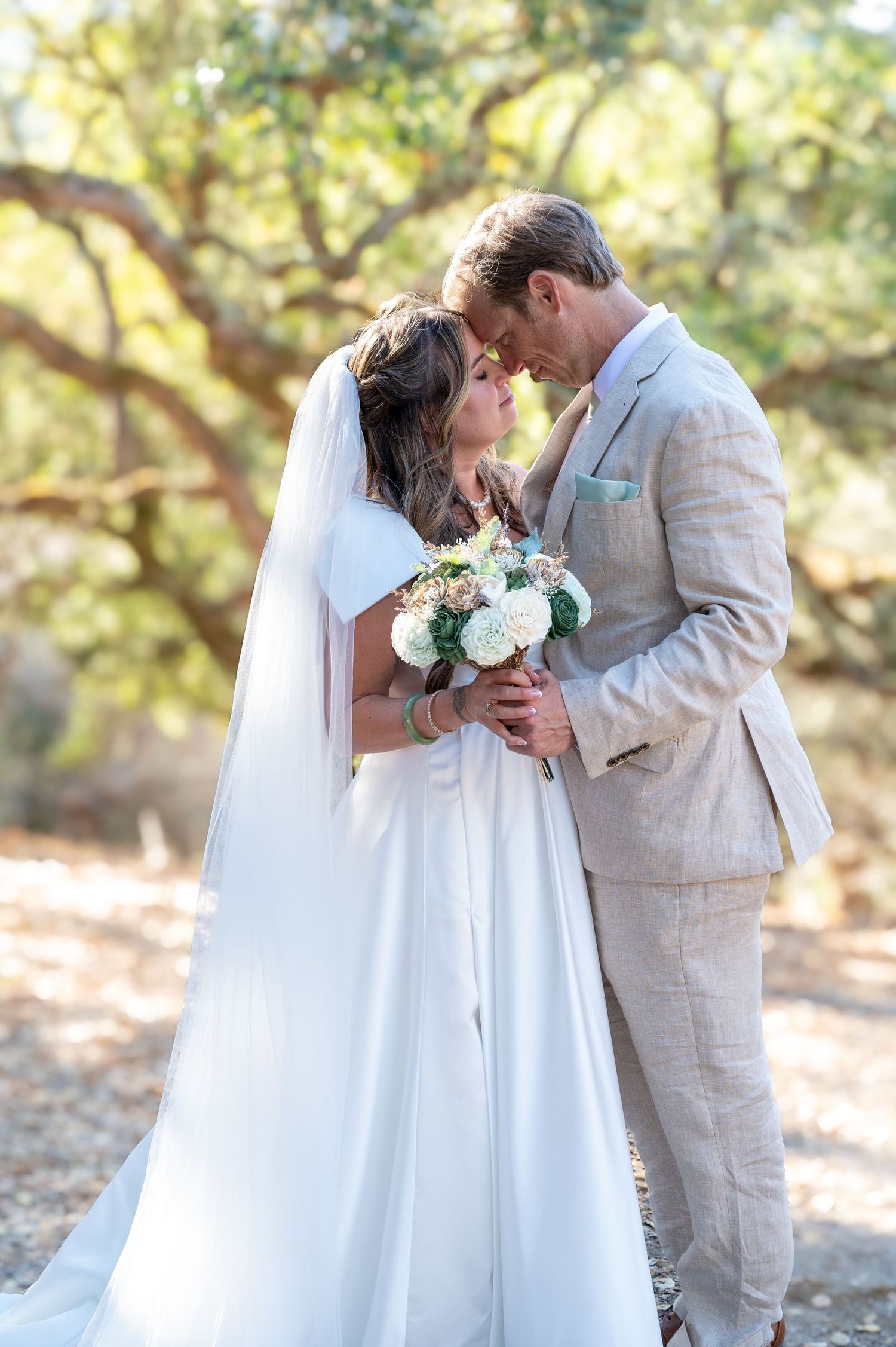 Carmel Valley Wedding A romantic wedding couple shares intimate moments in a natural outdoor setting with sunlit trees in the background.