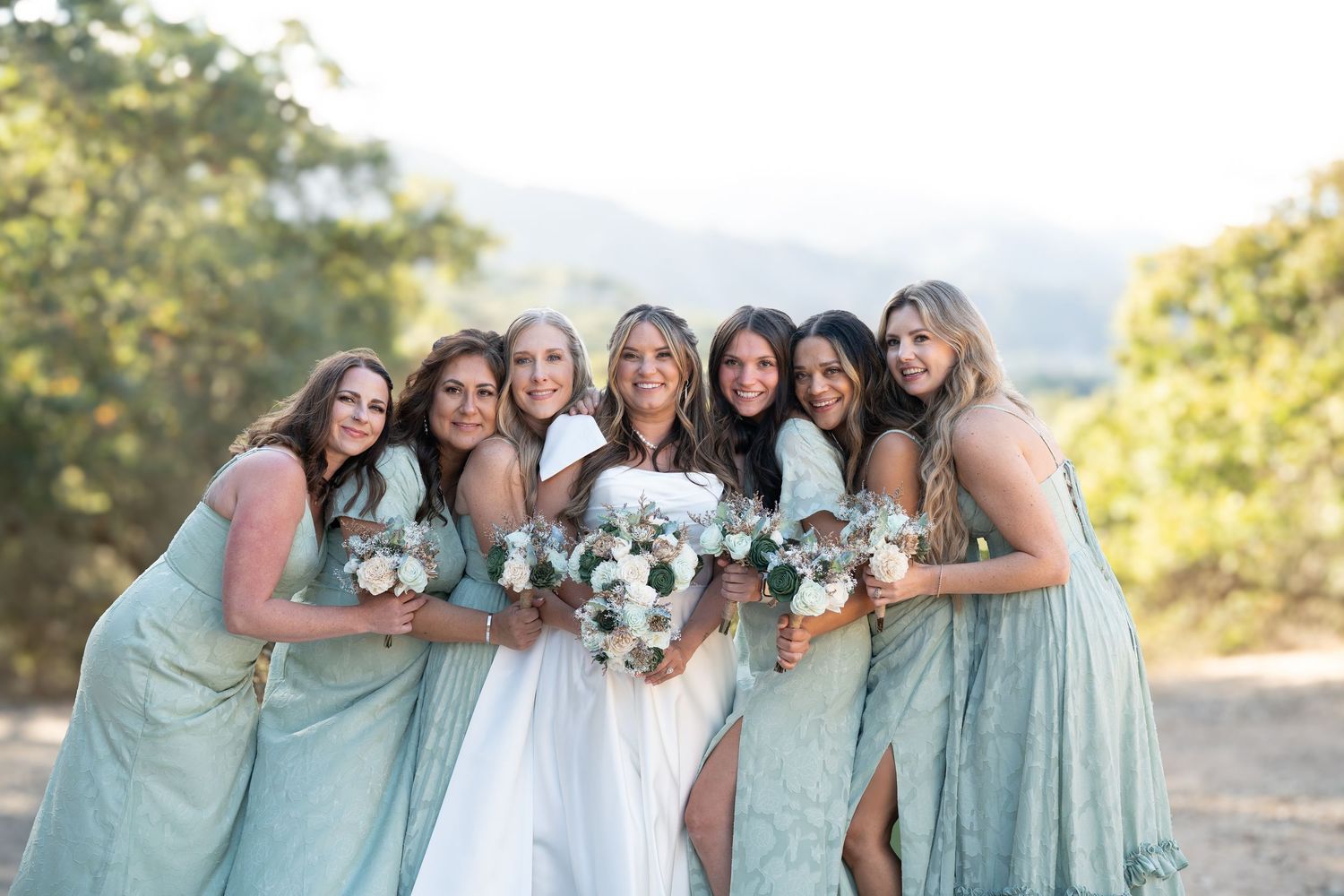 Wedding party in seafoam green dresses poses together outdoors in a scenic mountain setting.