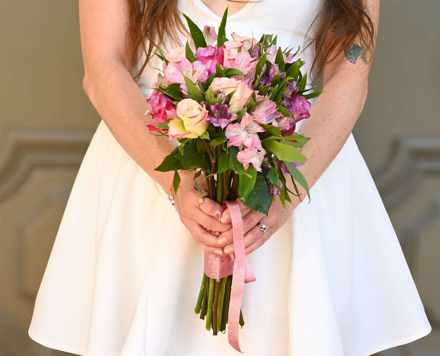 White bridal bouquet with pink and purple flowers held against a white dress.