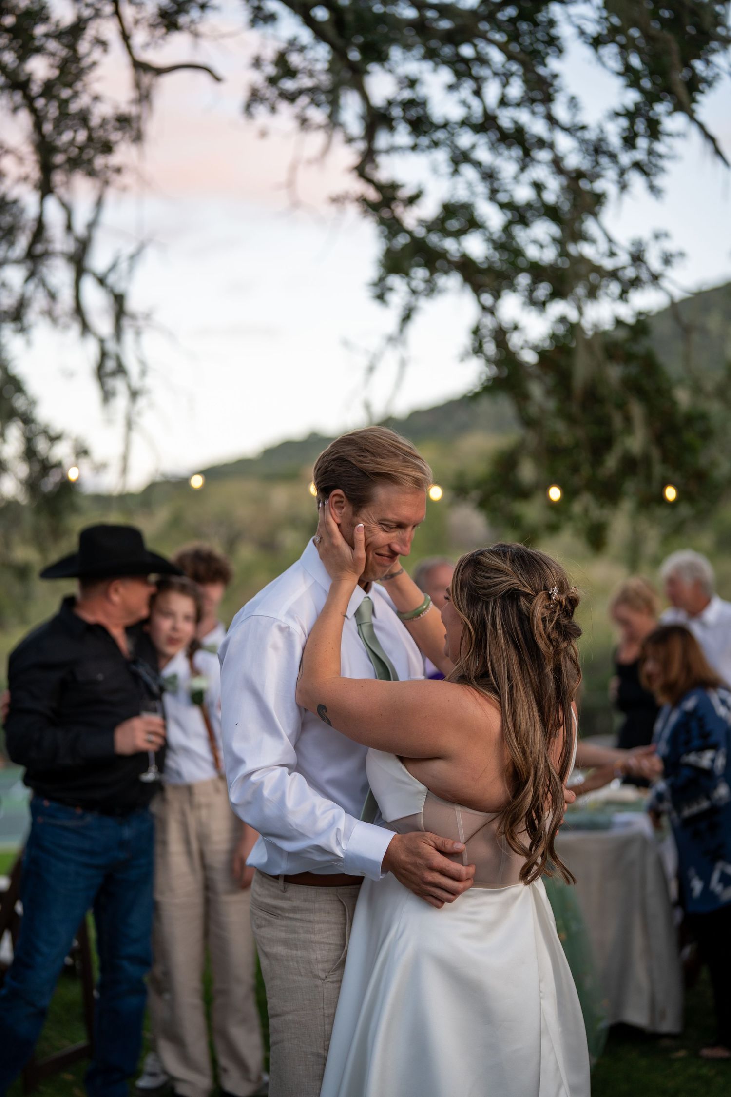 A romantic first dance sequence at an outdoor wedding reception with string lights and trees in the background.
