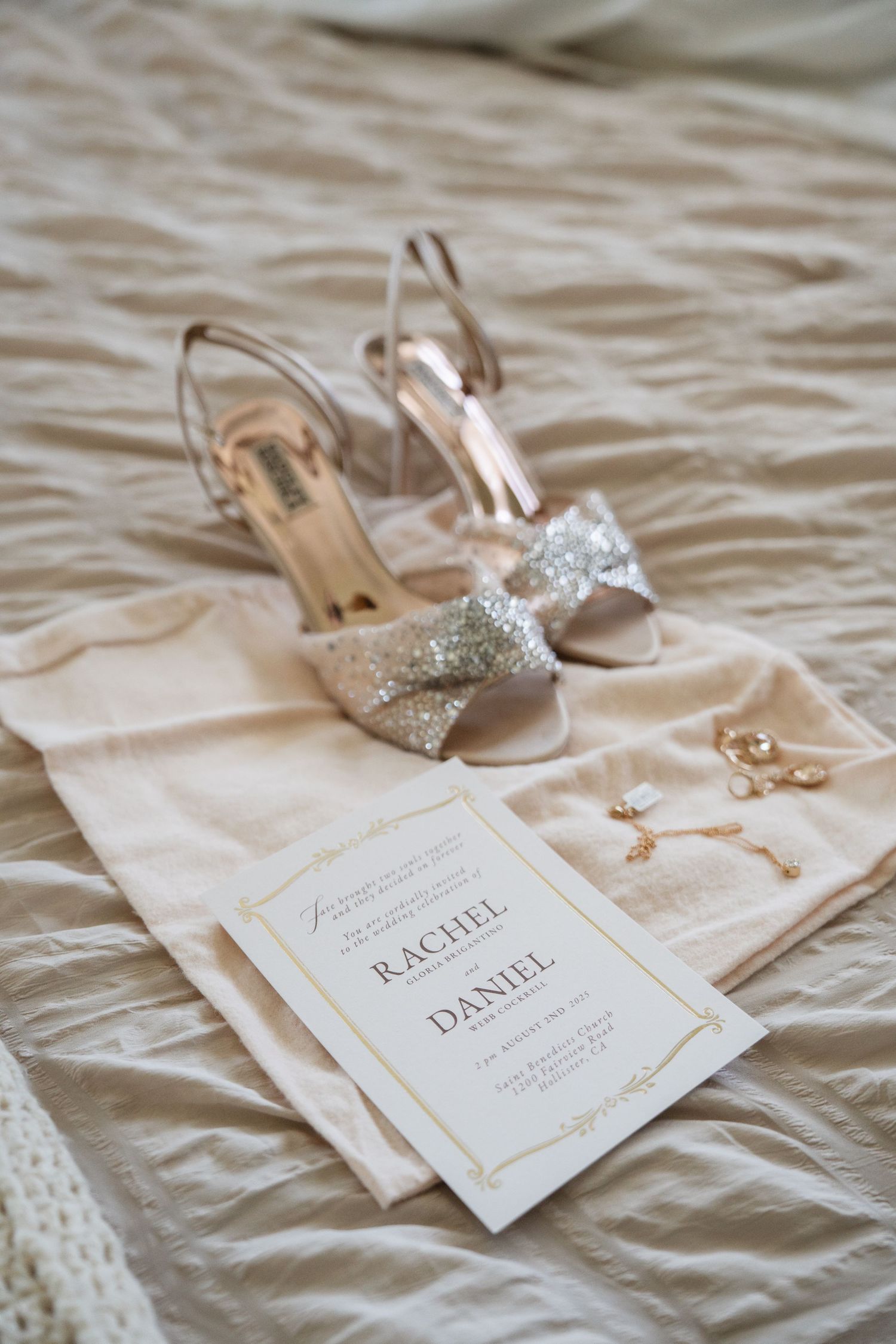 Wedding stationery and sparkly bridal shoes arranged on textured fabric.