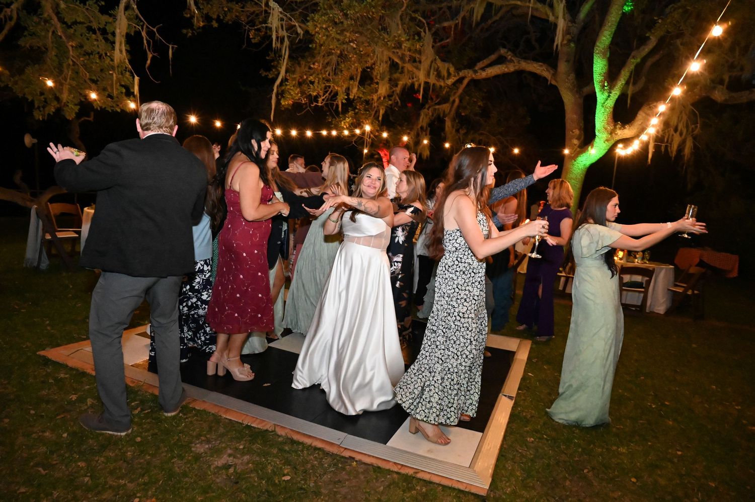 People dancing and celebrating at an outdoor evening wedding reception with string lights illuminating the festivities.