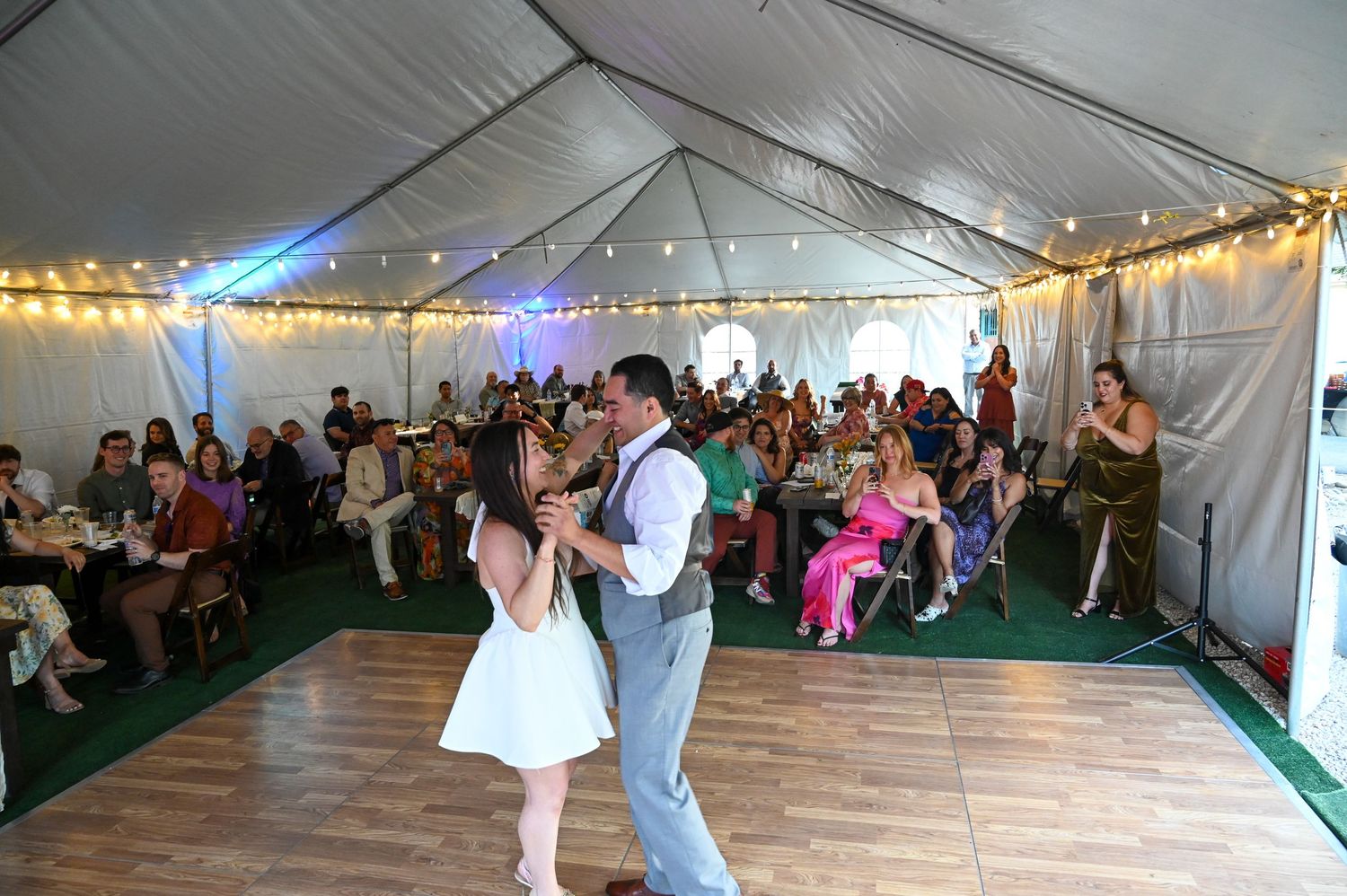 Wedding reception venue showing white tent interior with dance floor and seated guests.