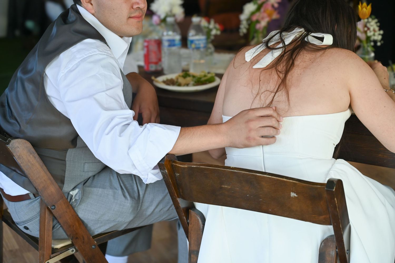 A couple signing documents at a wooden table in an outdoor setting.