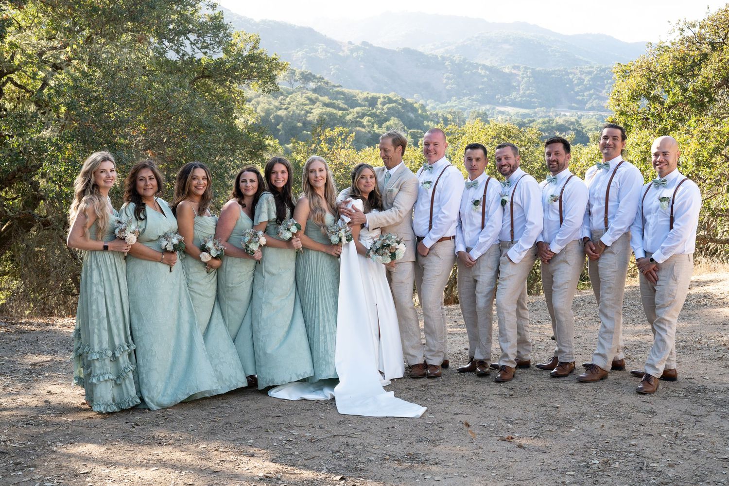 Wedding party in mint green dresses and khaki suits poses together on a hillside.
