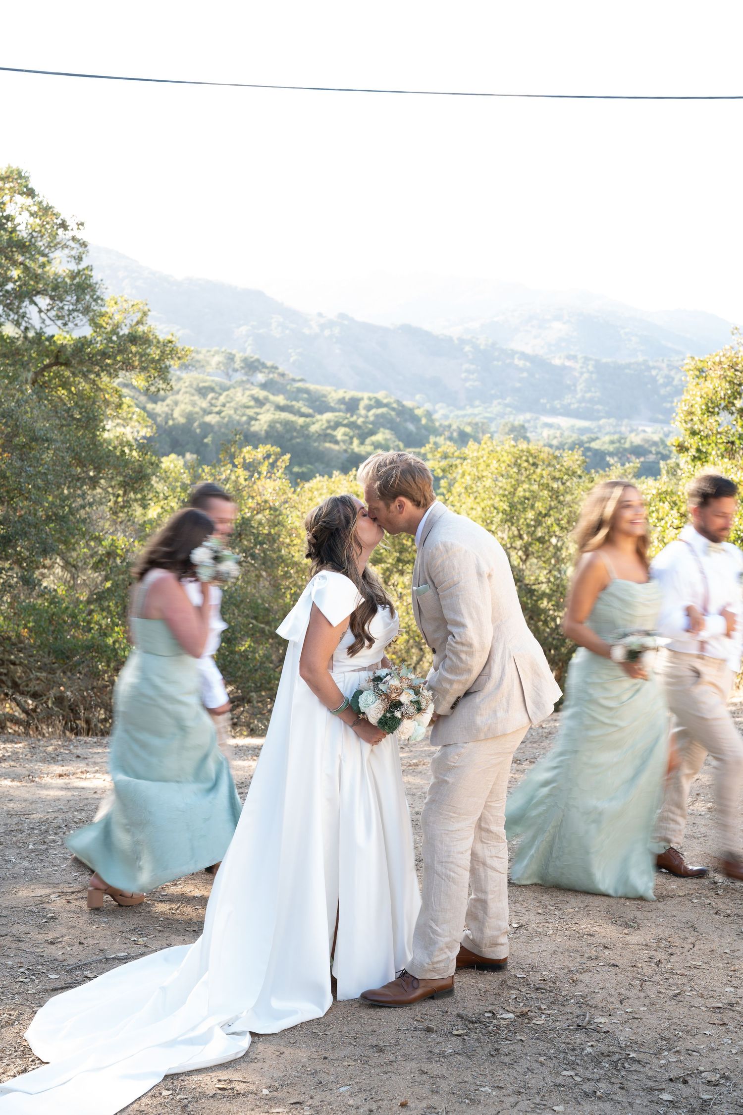 Carmel Valley Wedding Wedding party members in mint green dresses and light suits perform a playful falling domino sequence on a hilltop.