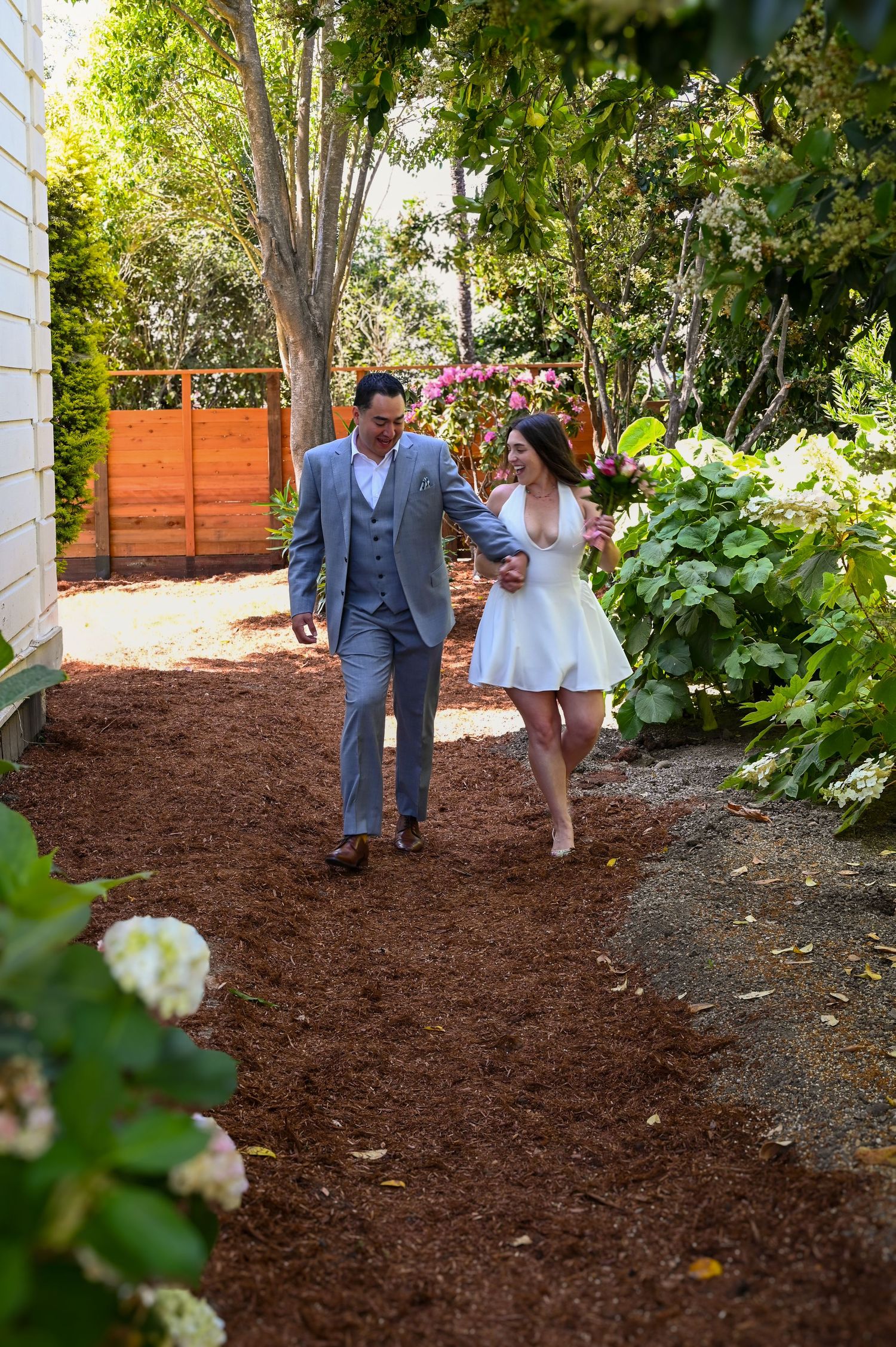 A couple walking along a garden path with mulch and greenery.