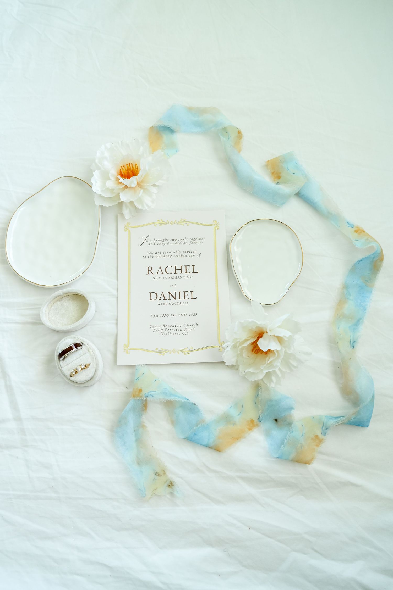 Wedding invitation suite with blue ribbon and floral accents on white background.