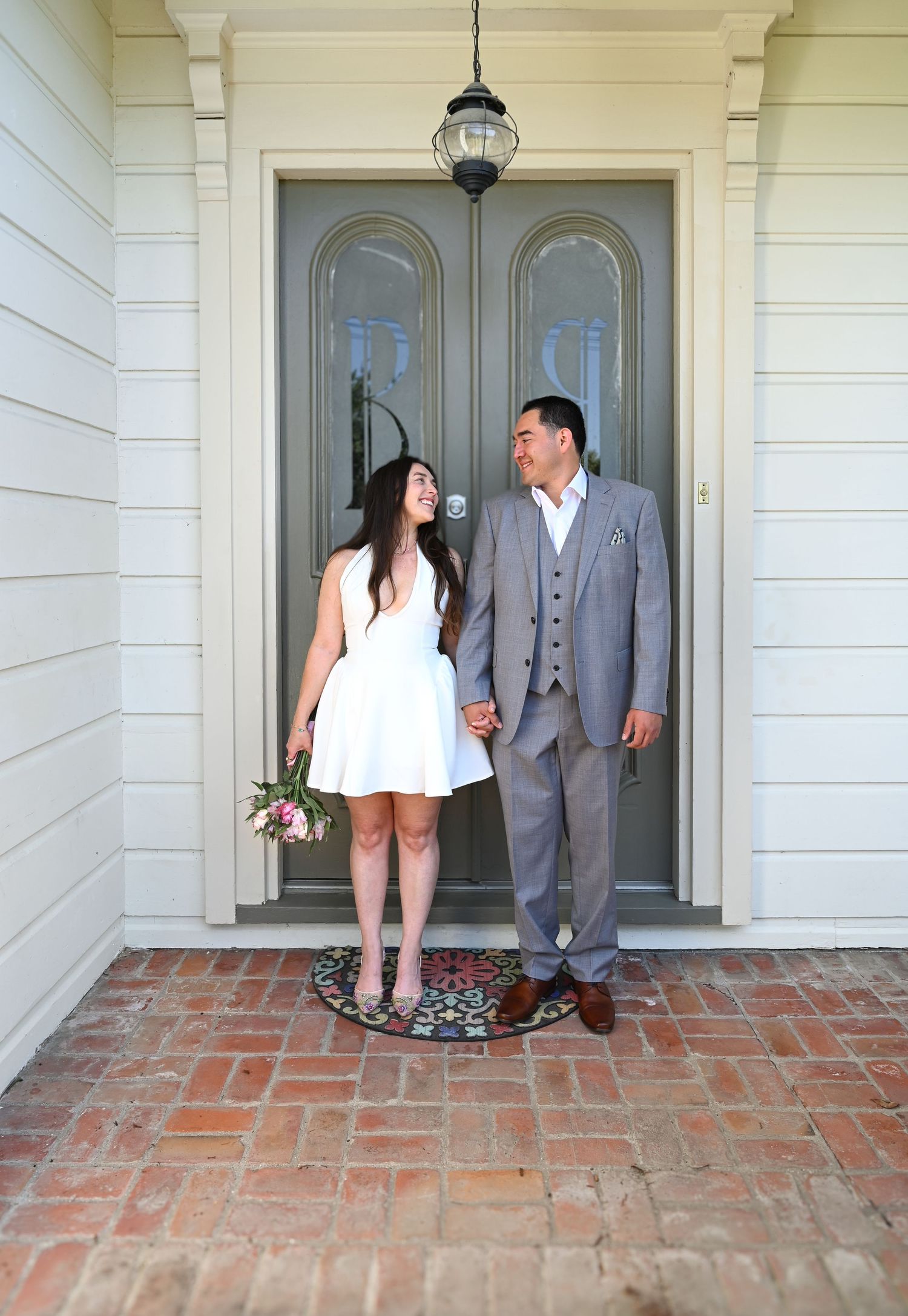 Bride and groom pose casually on brick porch of white colonial-style building.
