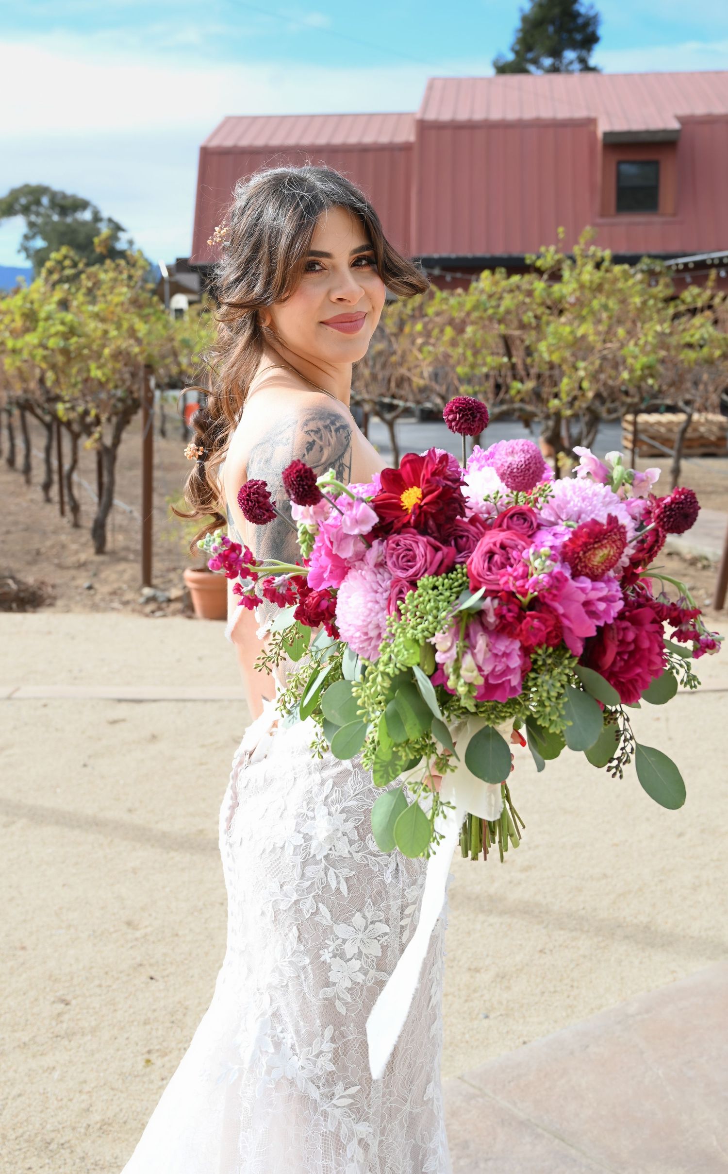 A stunning bridal bouquet featuring pink and burgundy flowers with greenery against a rustic outdoor setting.
