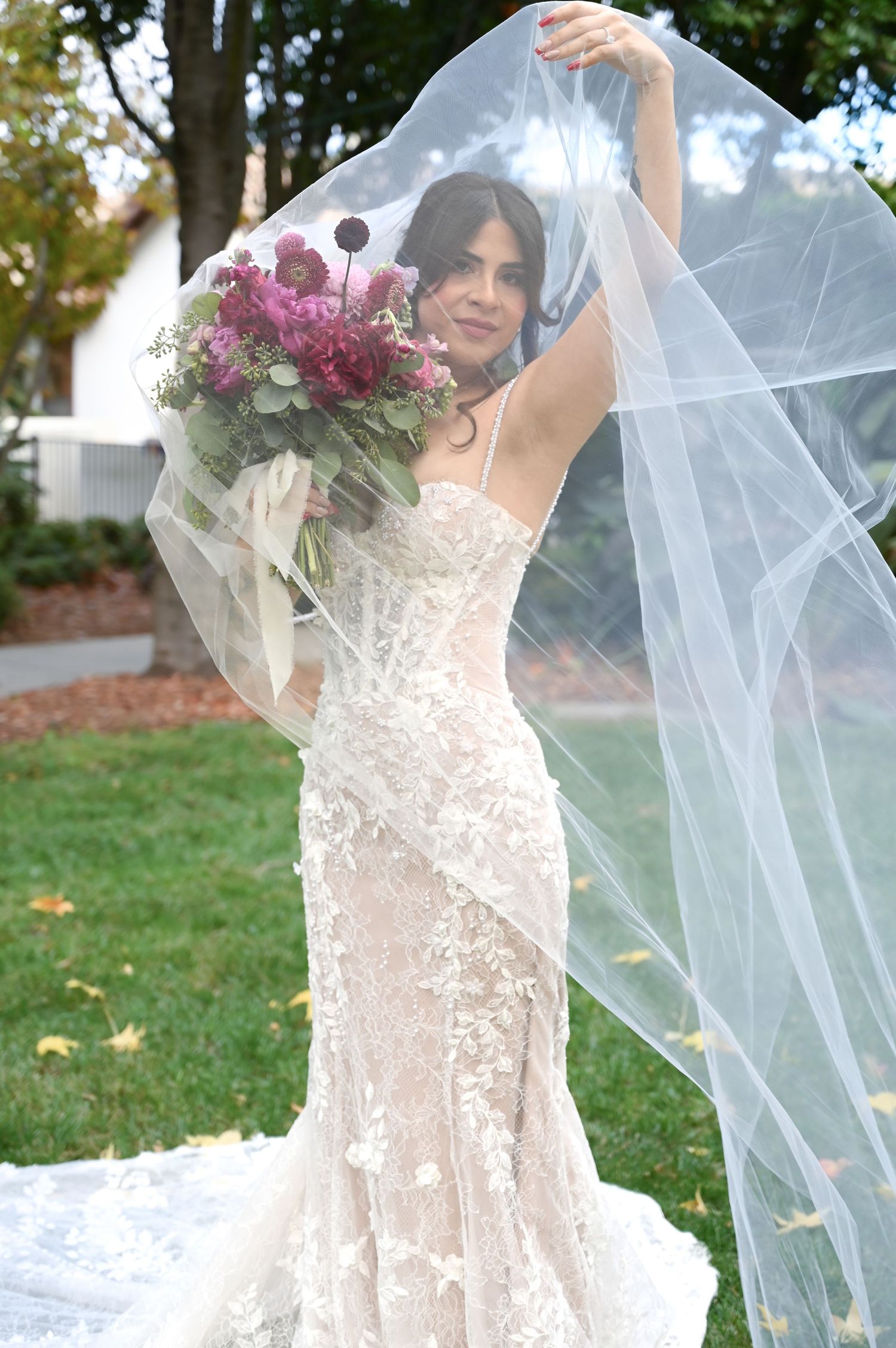 A flowing white wedding veil catches the breeze as it drapes gracefully on a grassy lawn.