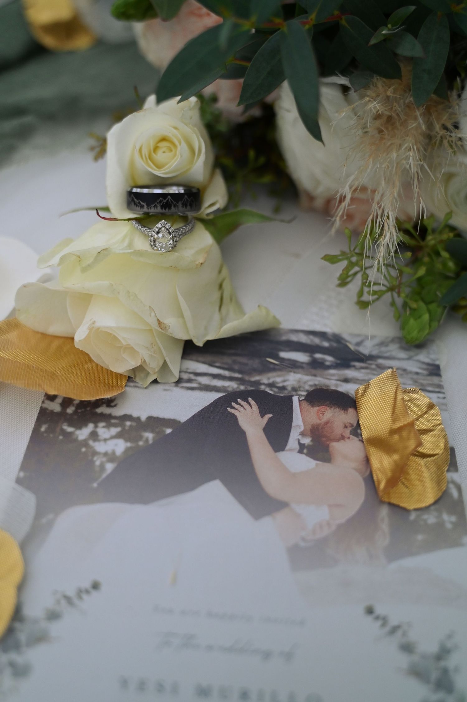 Wedding rings and white roses rest on a black and white photograph with delicate gold accents.