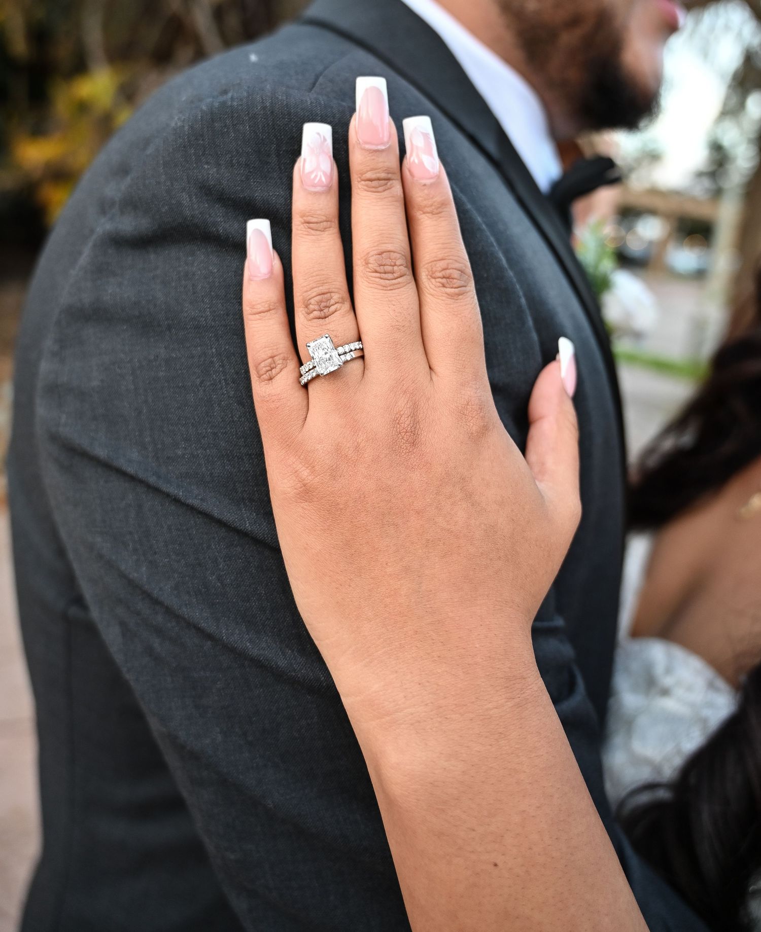 Close-up view of an engagement ring being displayed on a woman's hand against a dark suit background. Carmel Valley Wedding, California