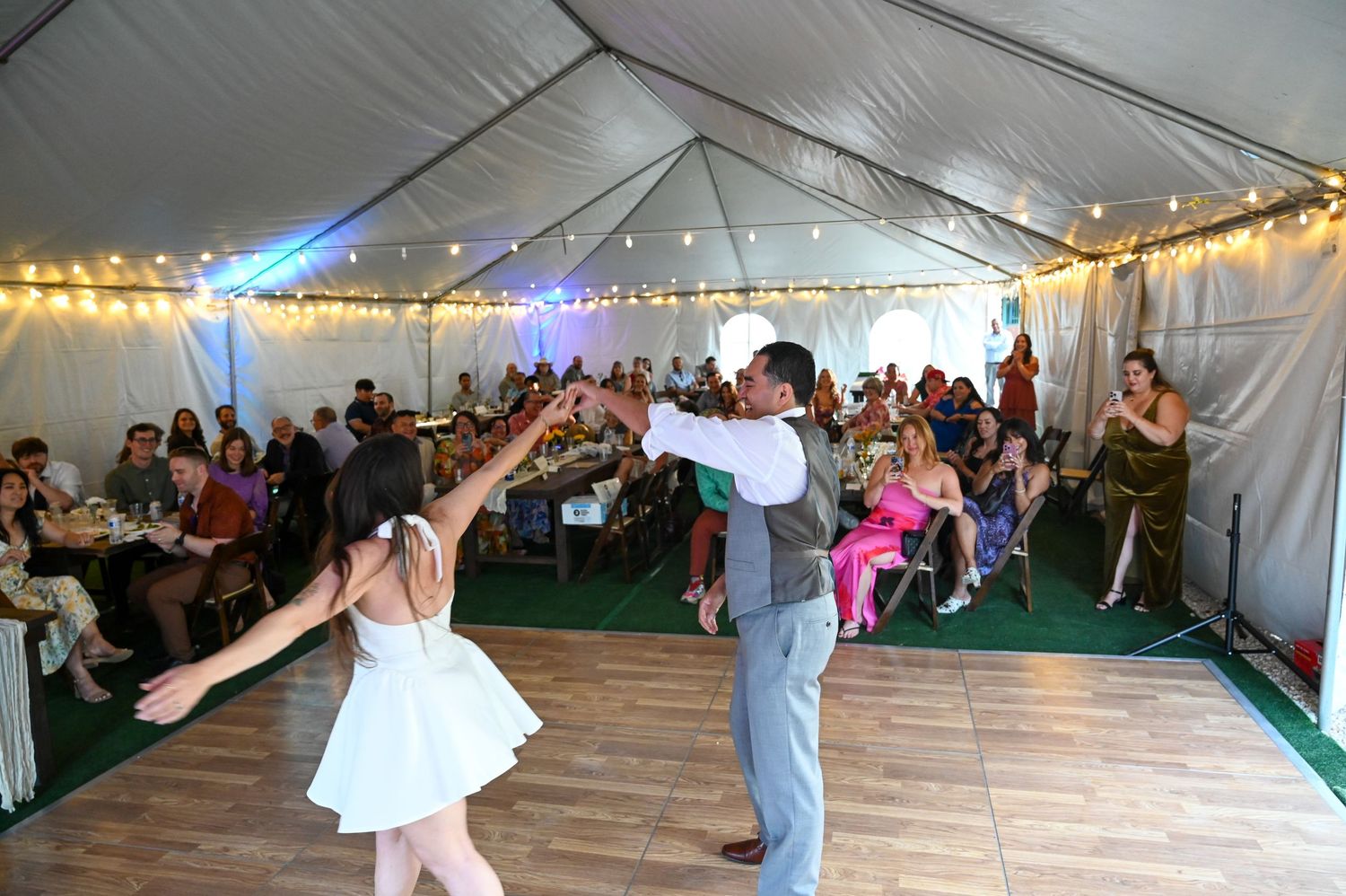 Wedding celebration in a spacious tent venue with guests dancing and mingling.
