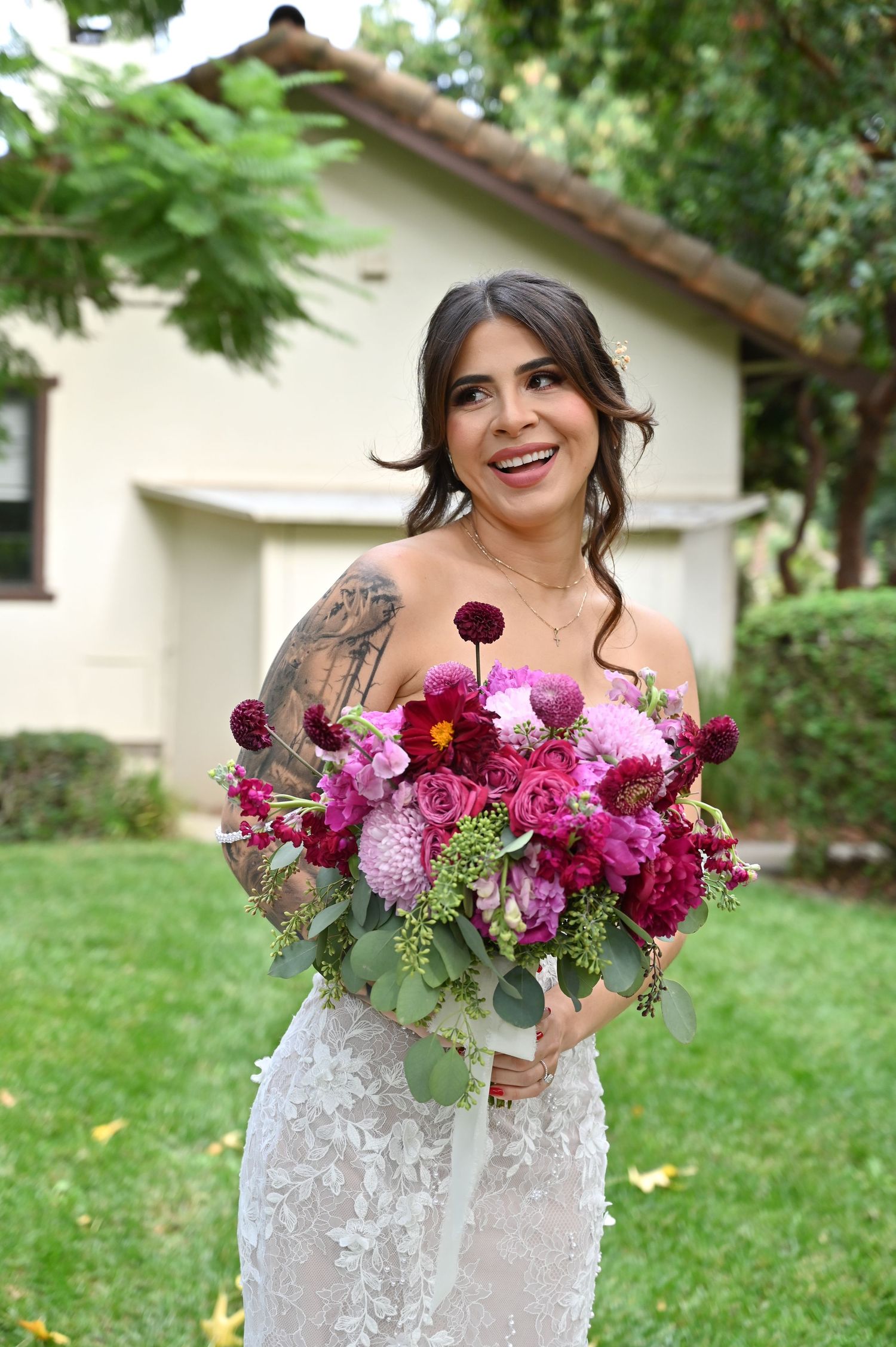 A joyful bridal portrait showcases a stunning floral arrangement with pink and burgundy blooms.