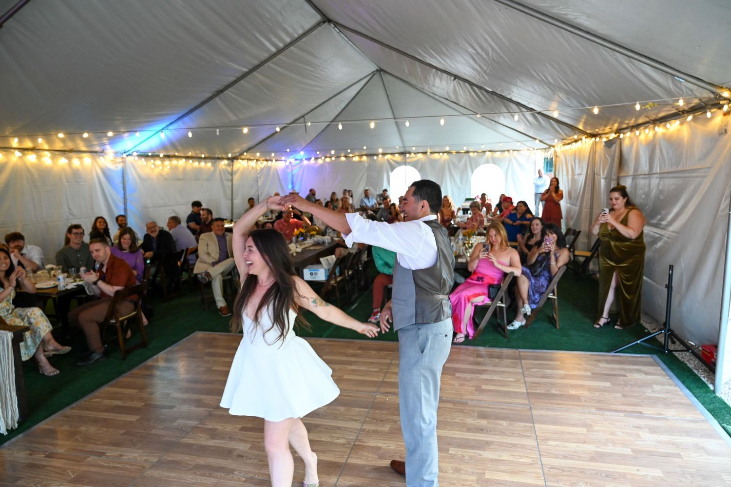 White tent wedding reception with dance floor and string lights illuminating the festive atmosphere.