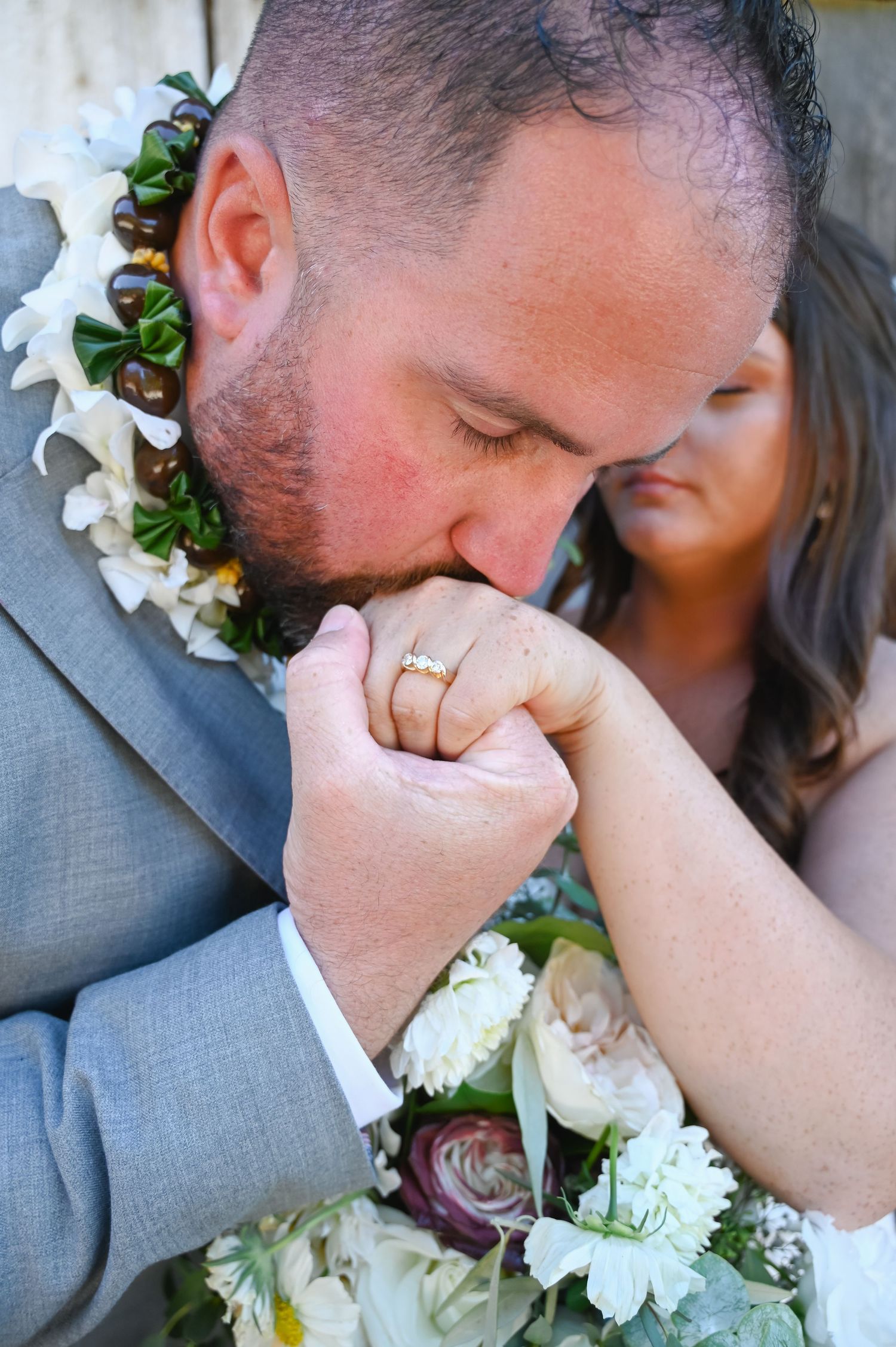 Romantic wedding portrait showing tender moment with white flowers and gray attire.