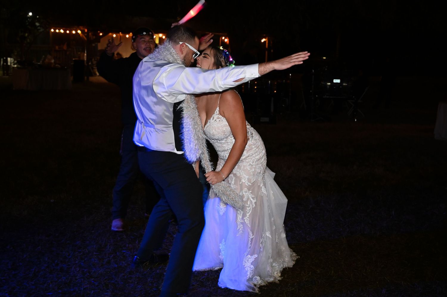 A couple dances together at a nighttime wedding reception, with the bride wearing a white lace gown.