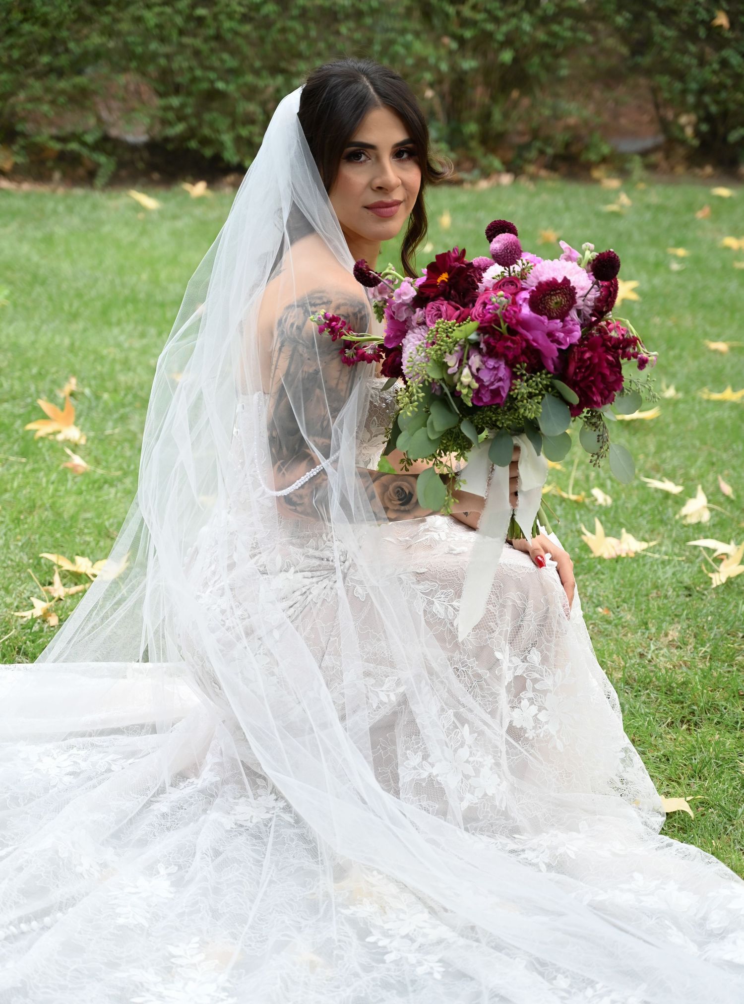 A romantic bridal portrait features a lace gown and flowing veil on a lawn with autumn leaves.